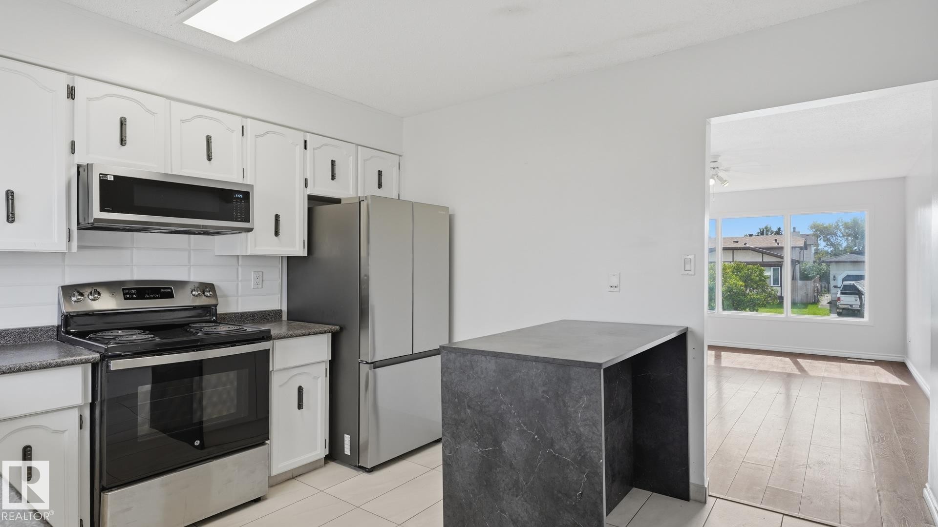Kitchen featuring white cabinetry, stainless steel appliances, a black countertop, and a built-in island - 12208 146 Avenue Nw, Edmonton, AB