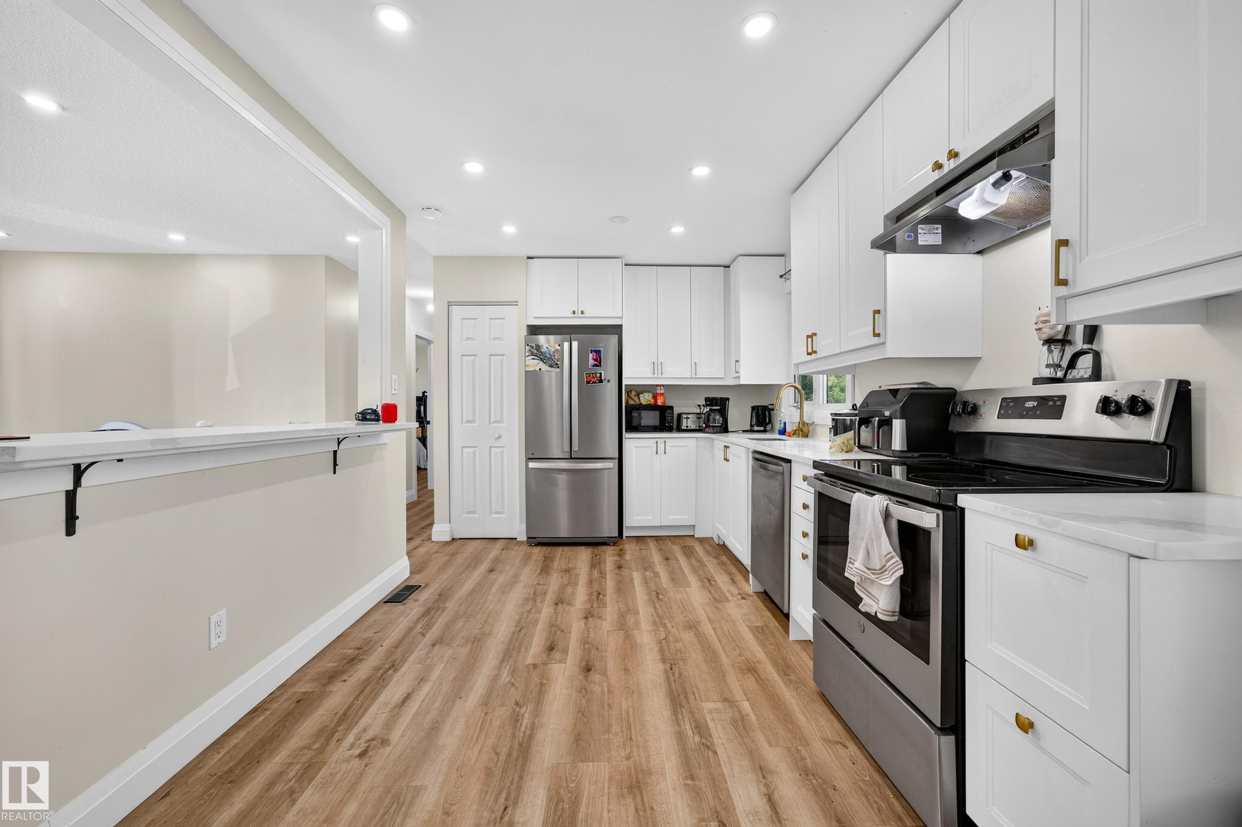 Kitchen featuring wood-finish flooring, white cabinetry, stainless steel appliances, and recessed lighting - 2412 80 Street Nw, Edmonton, AB