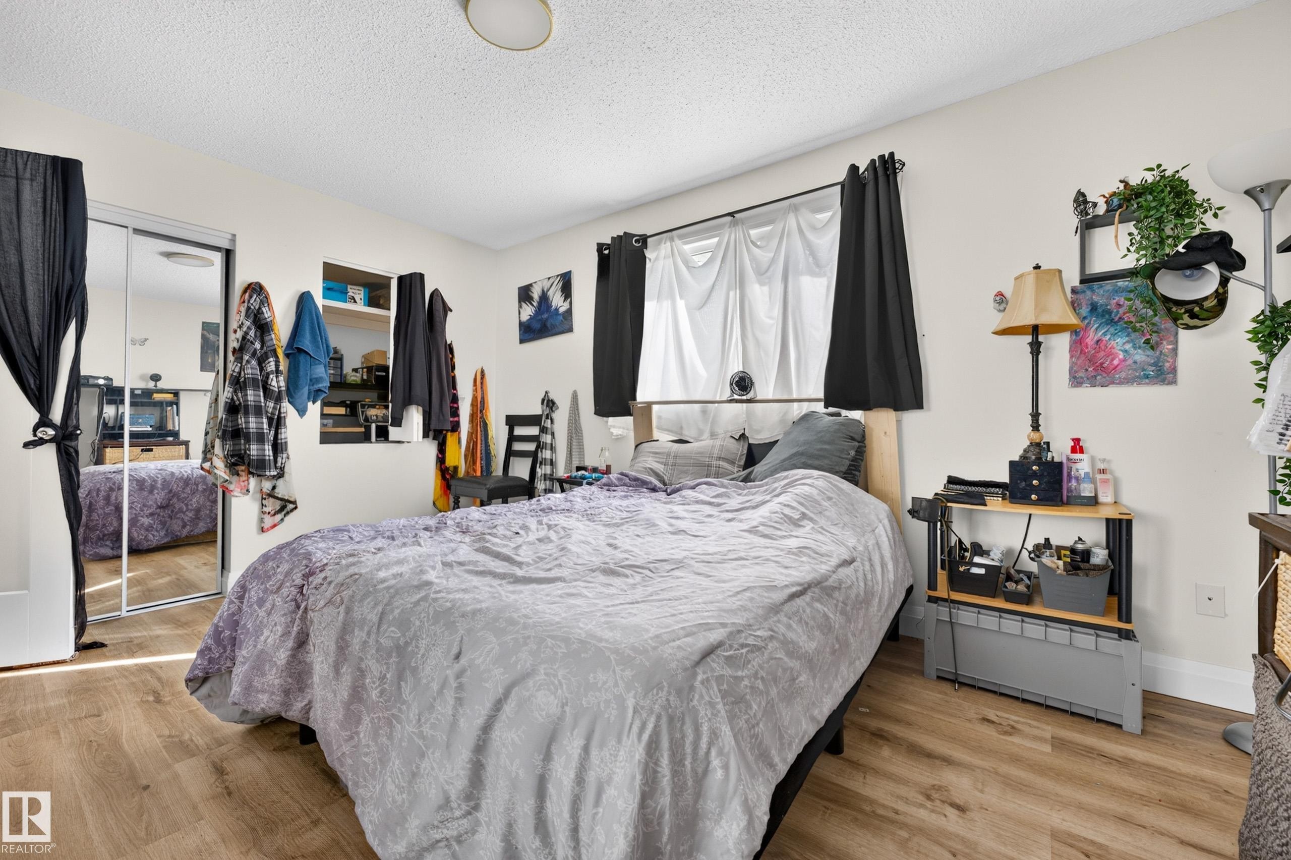 Wood-finish flooring, mirrored sliding closet doors, built-in wall shelving, and window with dark curtain panels - 2412 80 Street Nw, Edmonton, AB