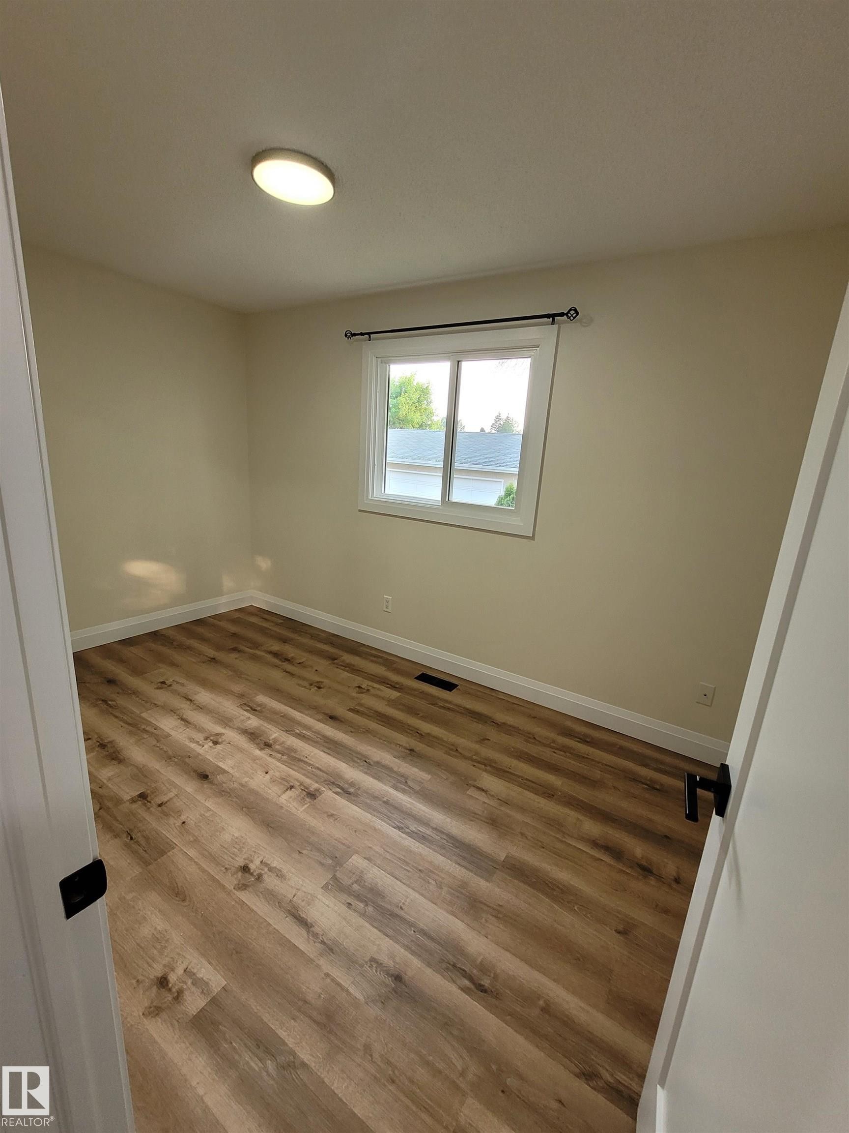 Neutral wall tones with wood-finish flooring, white trim, and a ceiling-mounted light fixture - 2412 80 Street Nw, Edmonton, AB