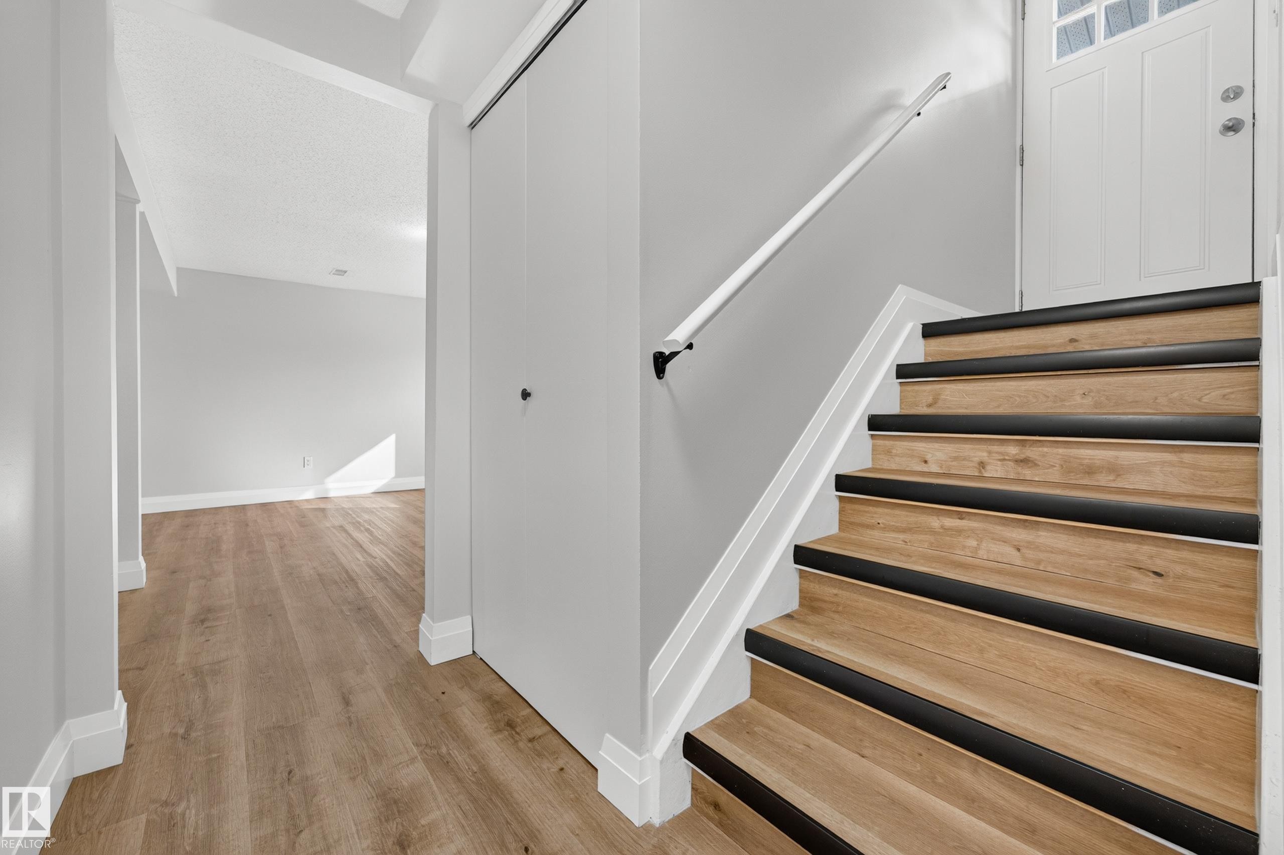 Wood-finish stairs with black tread accents and a white handrail - 2412 80 Street Nw, Edmonton, AB