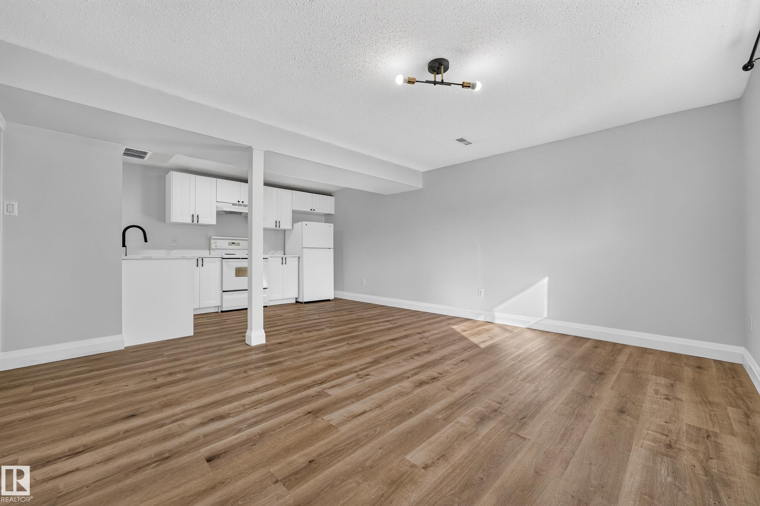 Open-concept living area featuring wood-finish flooring, white cabinetry, integrated appliances, a matte black gooseneck faucet, and contemporary ceiling lighting - 2412 80 Street Nw, Edmonton, AB