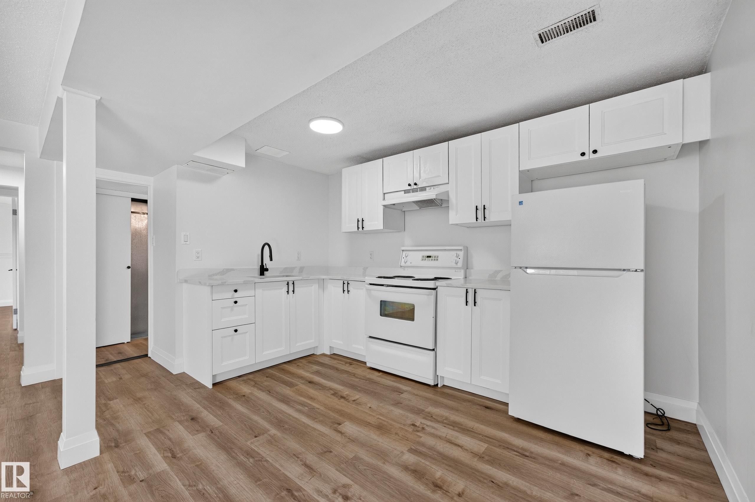 L-shaped kitchen featuring white cabinetry, light-toned countertops, and wood-finish flooring - 2412 80 Street Nw, Edmonton, AB
