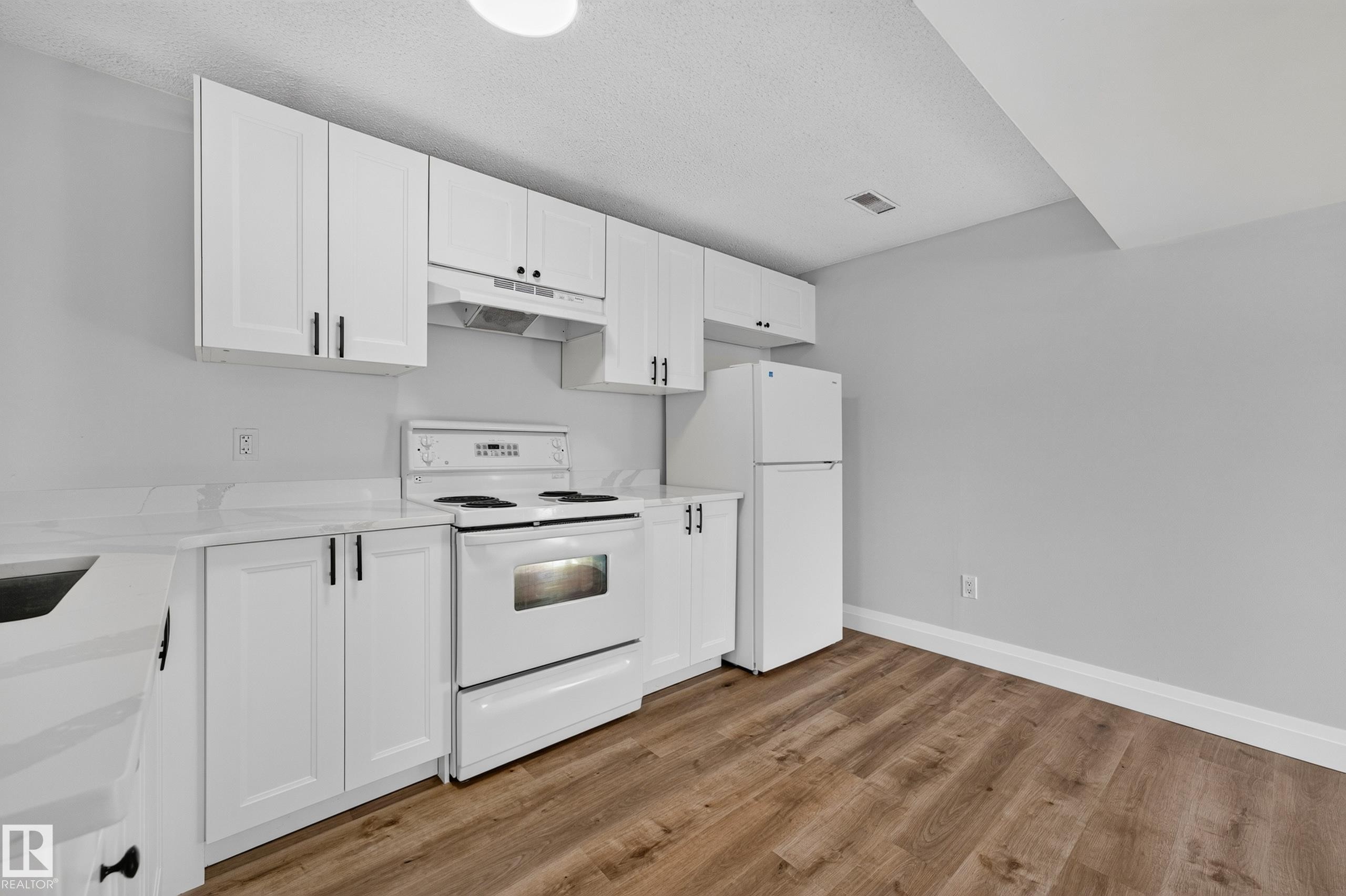 White shaker-style cabinetry with matte black hardware, white appliances, light-toned countertops, and wood-finish flooring - 2412 80 Street Nw, Edmonton, AB