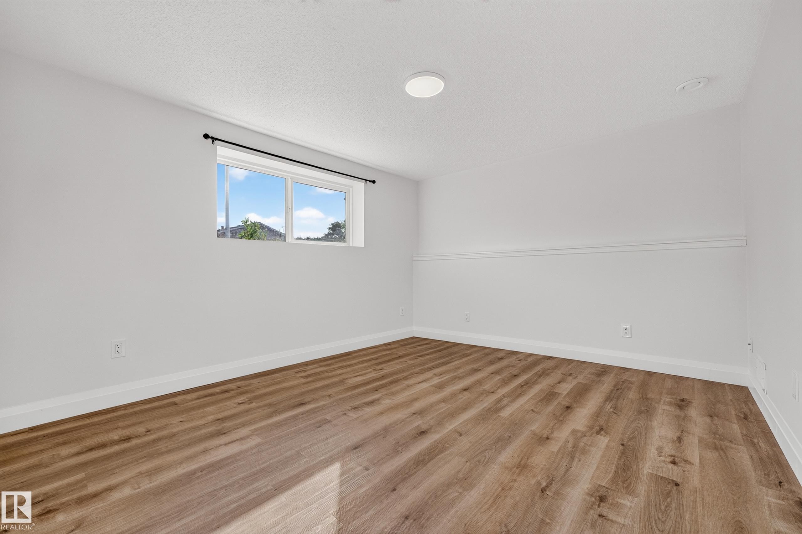 Wood-finish flooring, white painted walls, white trim, recessed lighting, and a window with a black curtain rod - 2412 80 Street Nw, Edmonton, AB