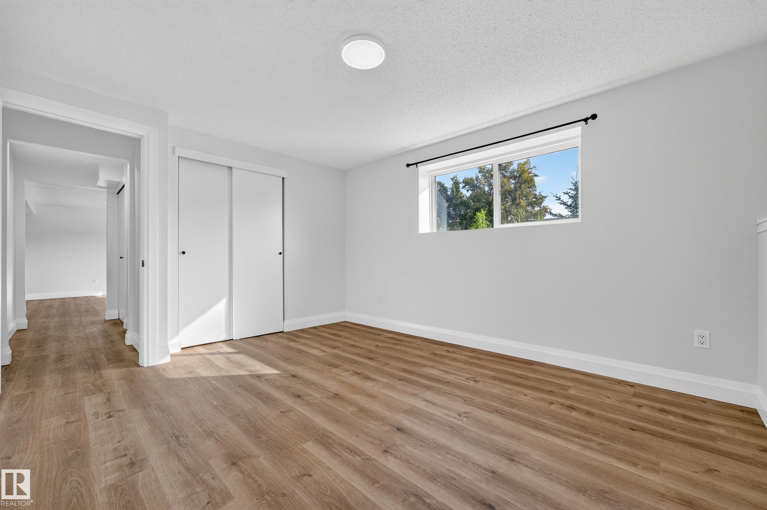 Wood-finish flooring throughout, white interior walls, and a window with exterior tree scenery - 2412 80 Street Nw, Edmonton, AB
