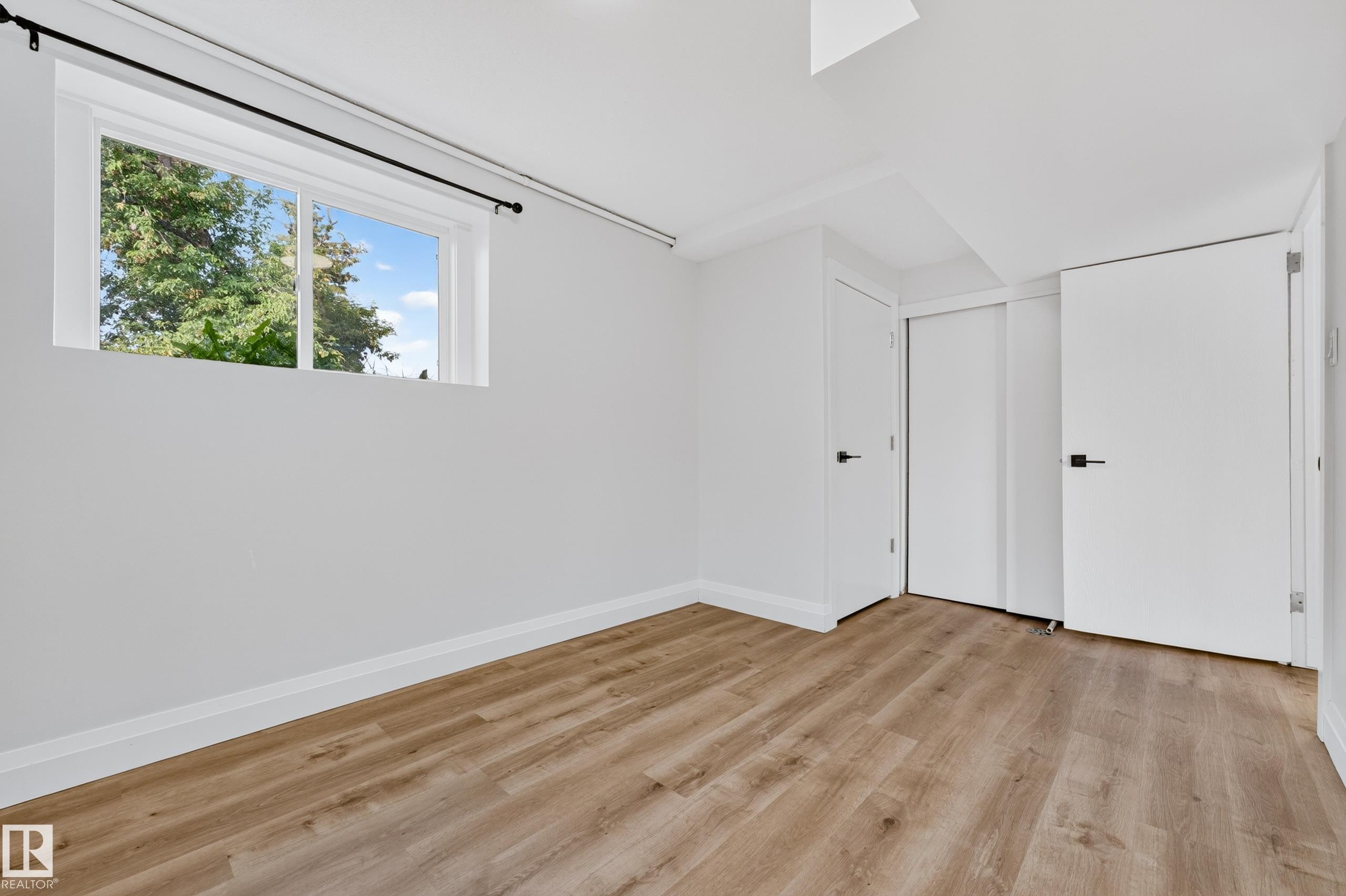 Room featuring wood-finish flooring, a white-framed window, and white interior doors with black hardware - 2412 80 Street Nw, Edmonton, AB