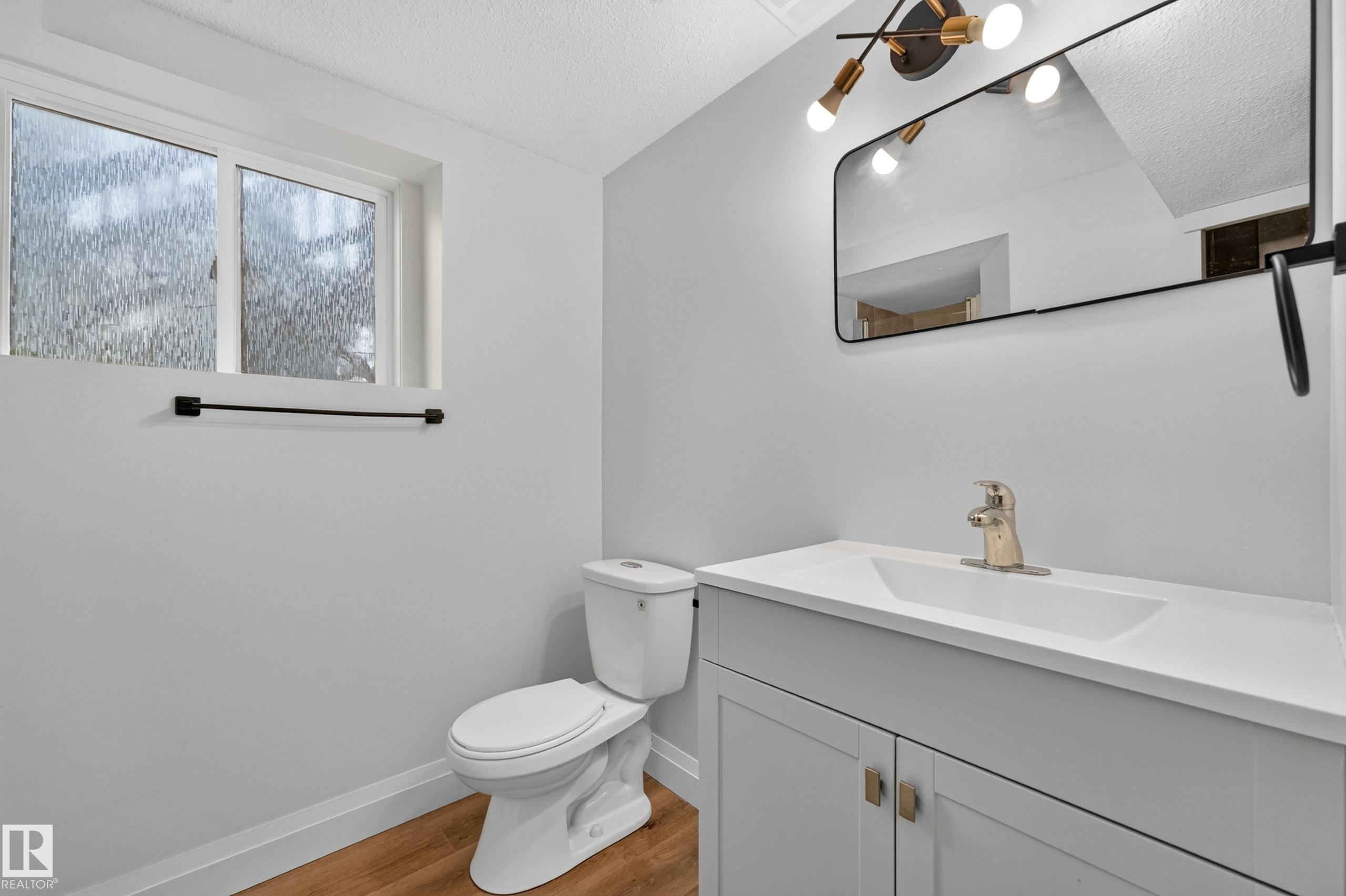 Vanity with integrated sink, gold-finish faucet, and modern light fixture - 2412 80 Street Nw, Edmonton, AB