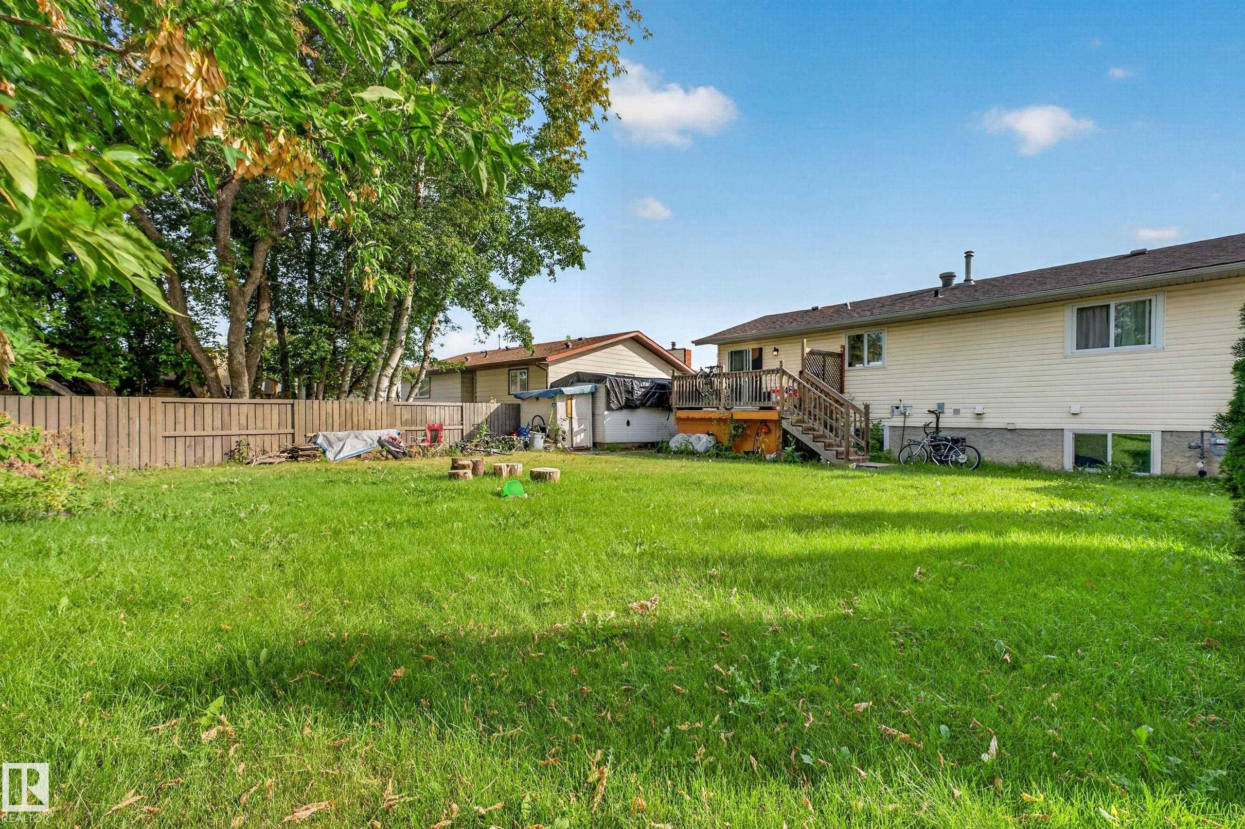 Expansive backyard featuring a large green lawn, wood fence, and a multi-level wood deck with stairs - 2412 80 Street Nw, Edmonton, AB