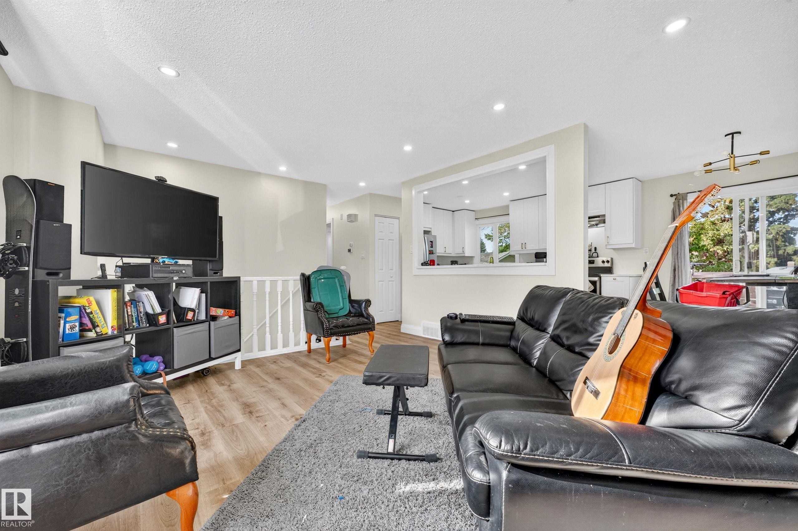 Recessed ceiling lighting, wood-finish flooring, white wall paint, and a pass-through opening to the kitchen featuring white cabinetry - 2412 80 Street Nw, Edmonton, AB