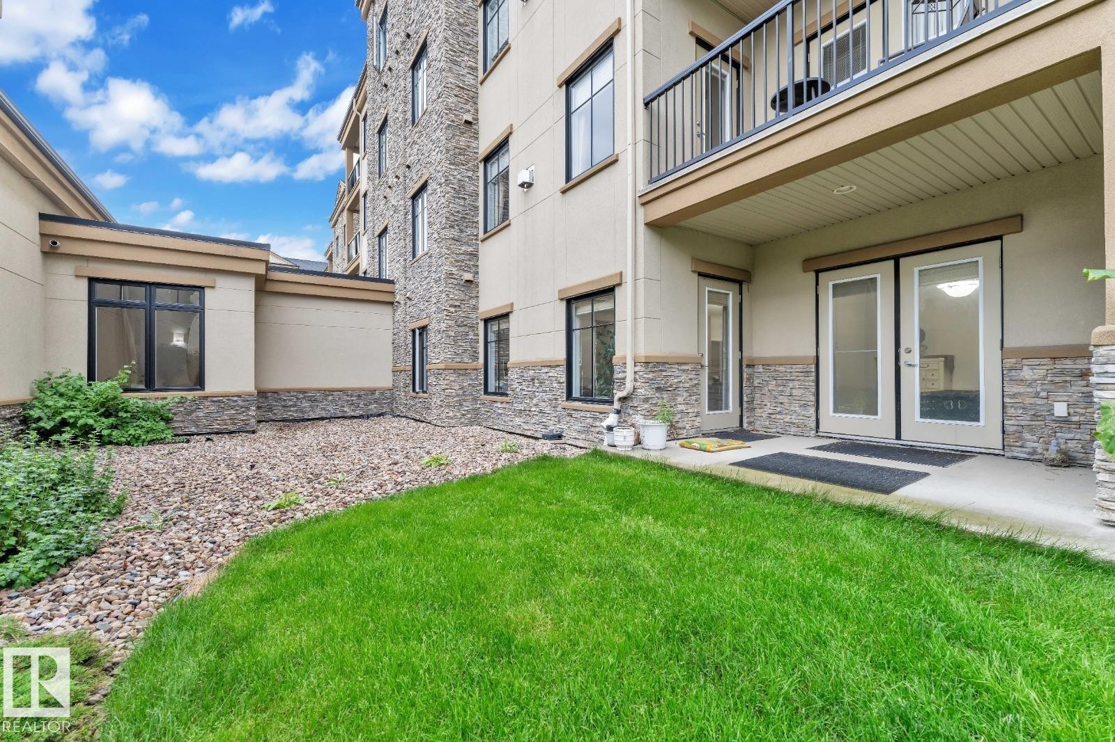Building exterior featuring stacked stone accents, stucco siding, and multiple windows - #105 160 Magrath Rd Nw, Edmonton, AB