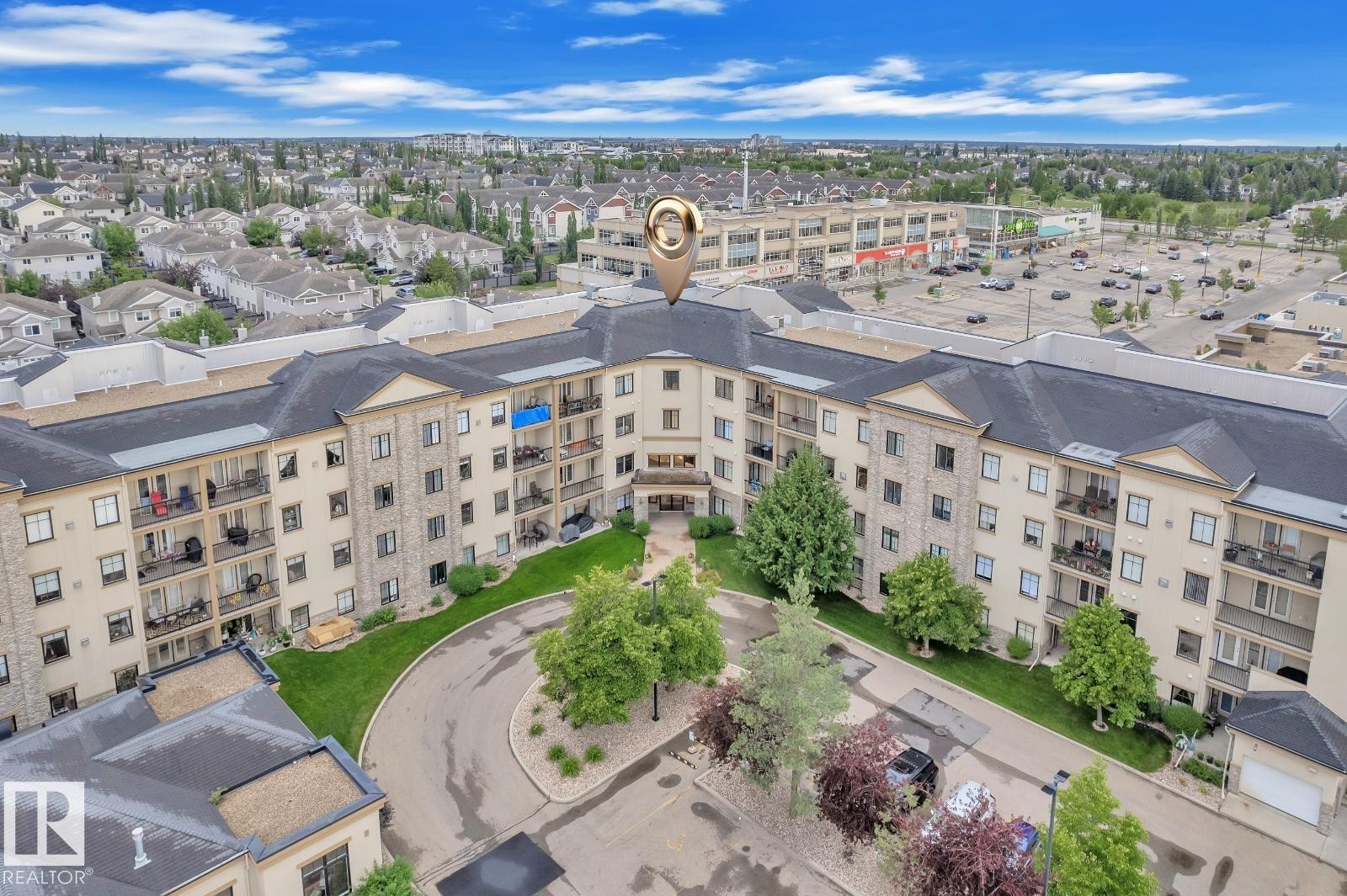 Multi-story residential building featuring stone and stucco exterior, individual balconies, and a paved circular driveway - #105 160 Magrath Rd Nw, Edmonton, AB