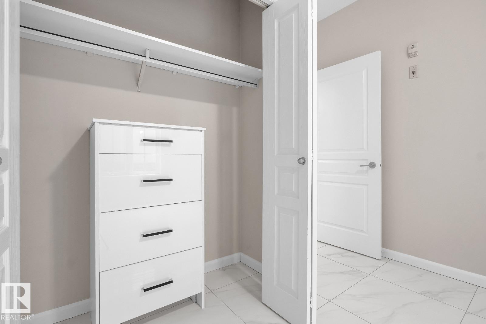 Walk-in closet with white shelving and a hanging rod, complemented by neutral wall tones - #105 160 Magrath Rd Nw, Edmonton, AB