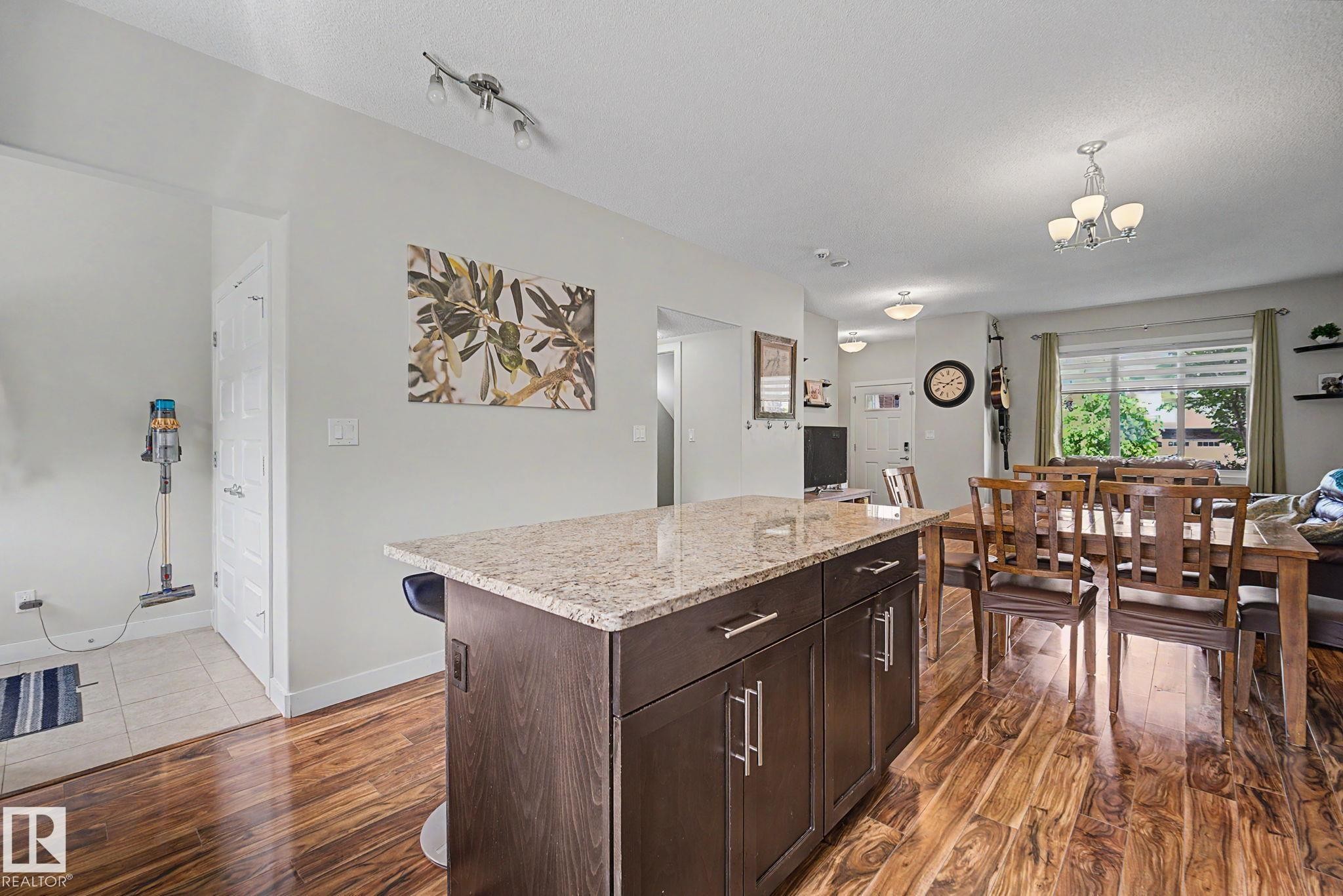 Kitchen island featuring a granite-style countertop and dark wood-finish cabinetry with silver-tone hardware - 3343 Weidle Way Sw, Edmonton, AB
