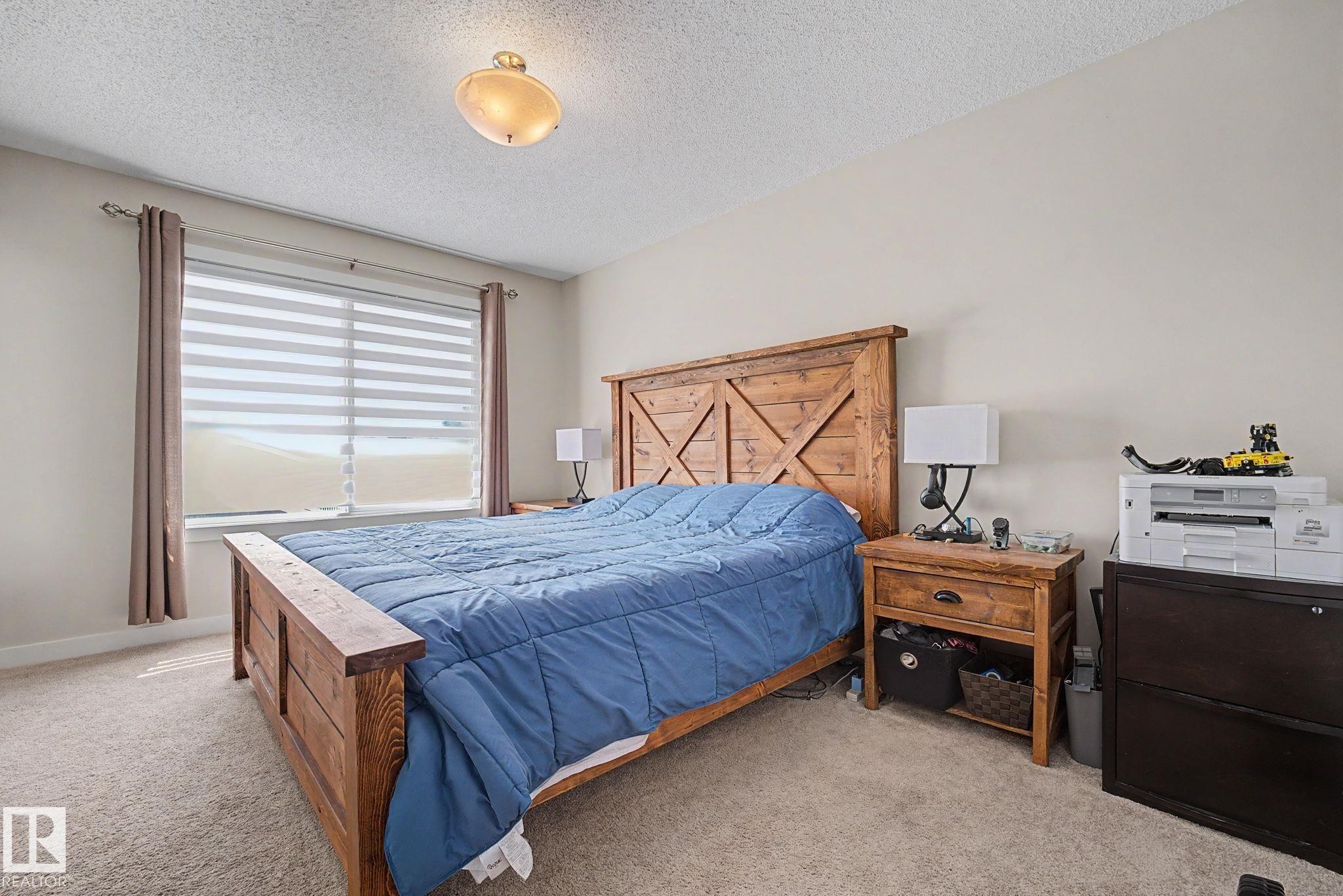Window with horizontal blinds and drapes, light neutral wall paint, textured ceiling, and neutral carpet - 3343 Weidle Way Sw, Edmonton, AB
