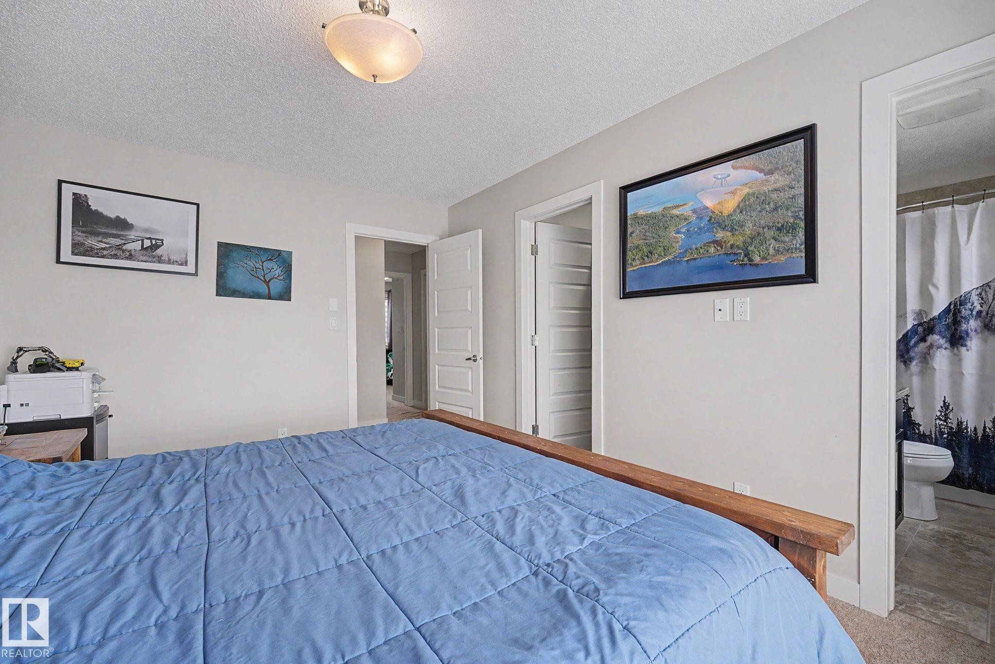 Bedroom featuring light neutral wall paint, wood-finish flooring, a flush-mount ceiling light fixture, and a white interior door - 3343 Weidle Way Sw, Edmonton, AB