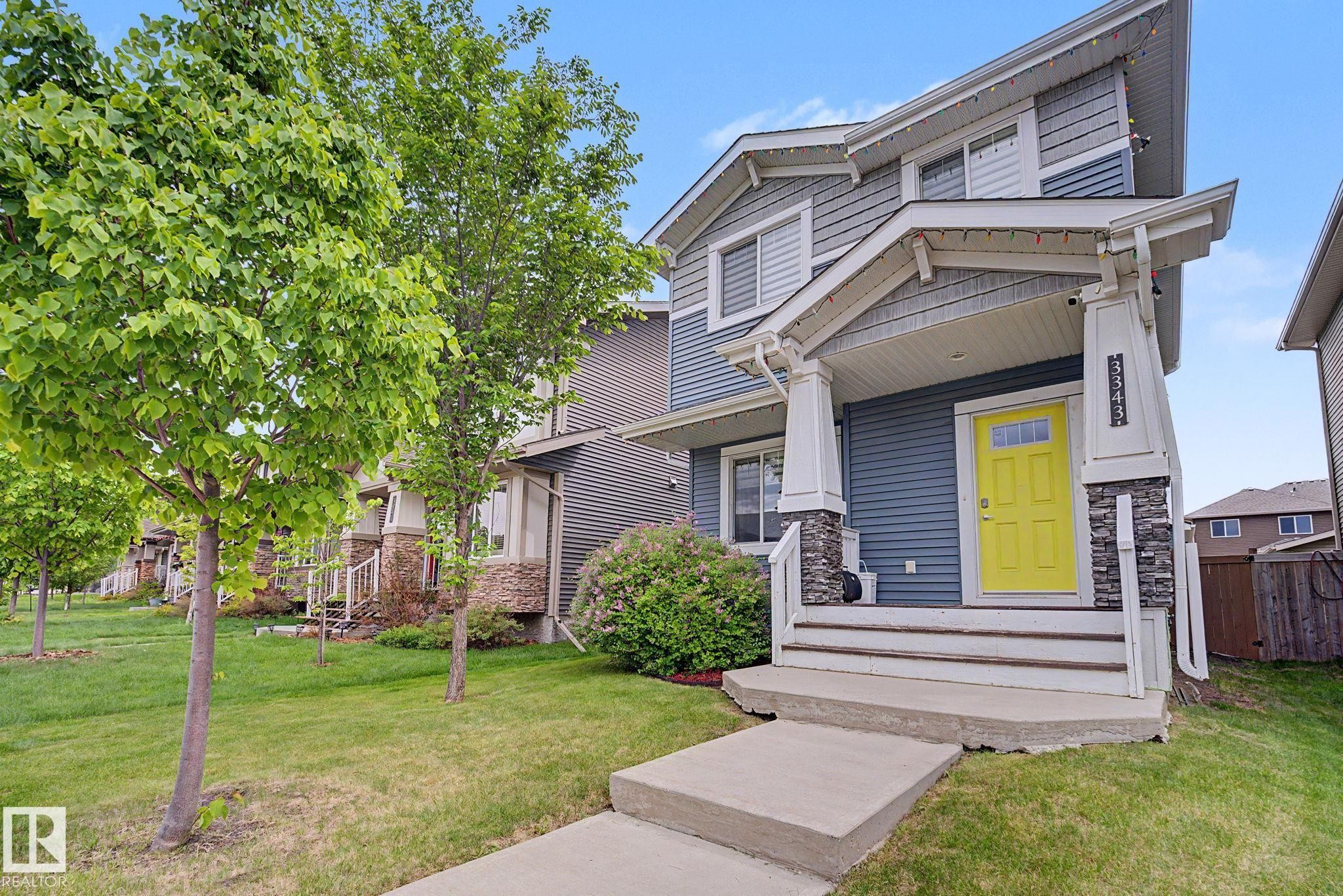 Contemporary facade featuring blue horizontal siding, grey shake siding, stone column accents, and a vibrant yellow entry door with transom window - 3343 Weidle Way Sw, Edmonton, AB