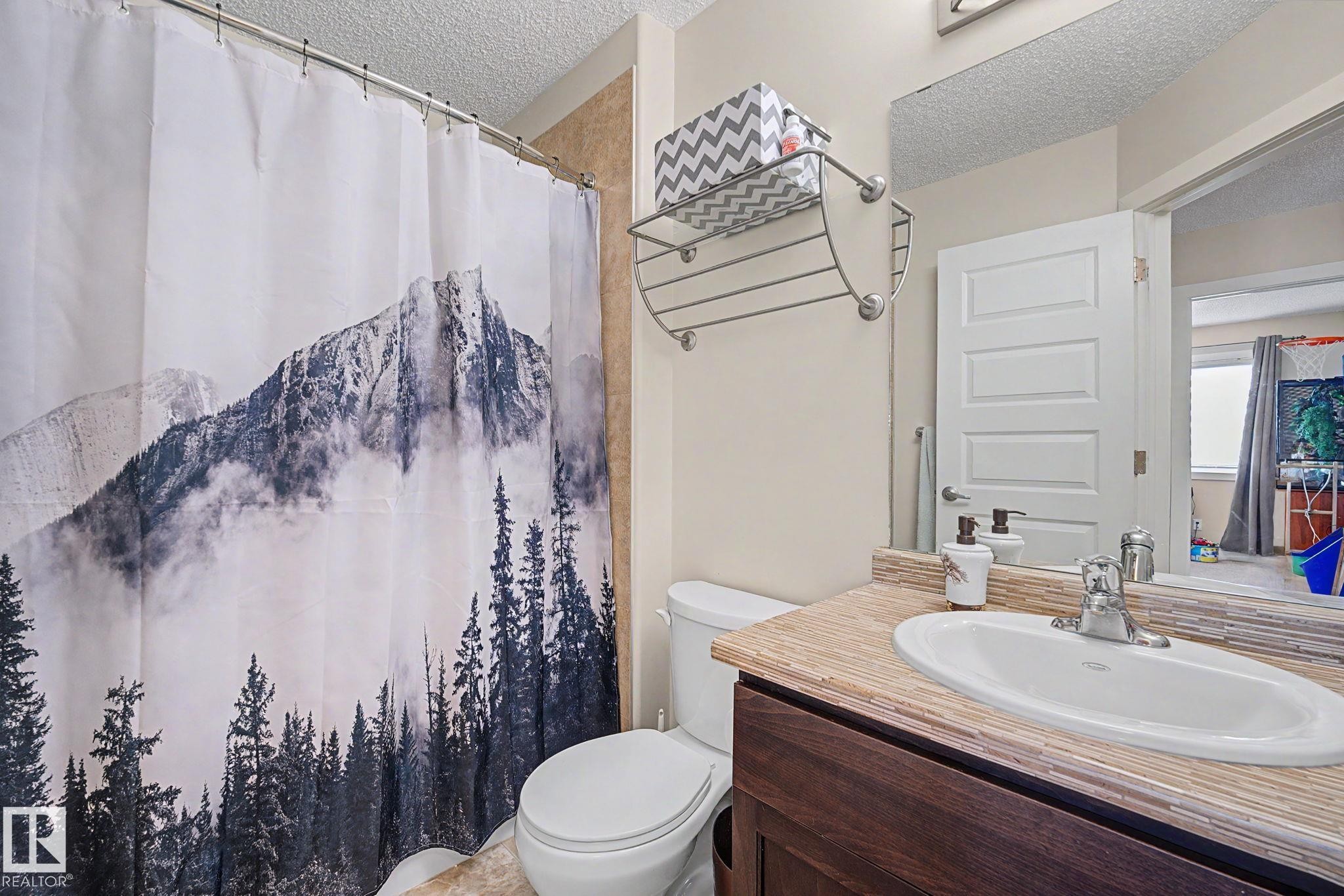 Bathroom featuring a dark wood-finish vanity with an integrated sink, chrome faucet, and a textured countertop - 3343 Weidle Way Sw, Edmonton, AB
