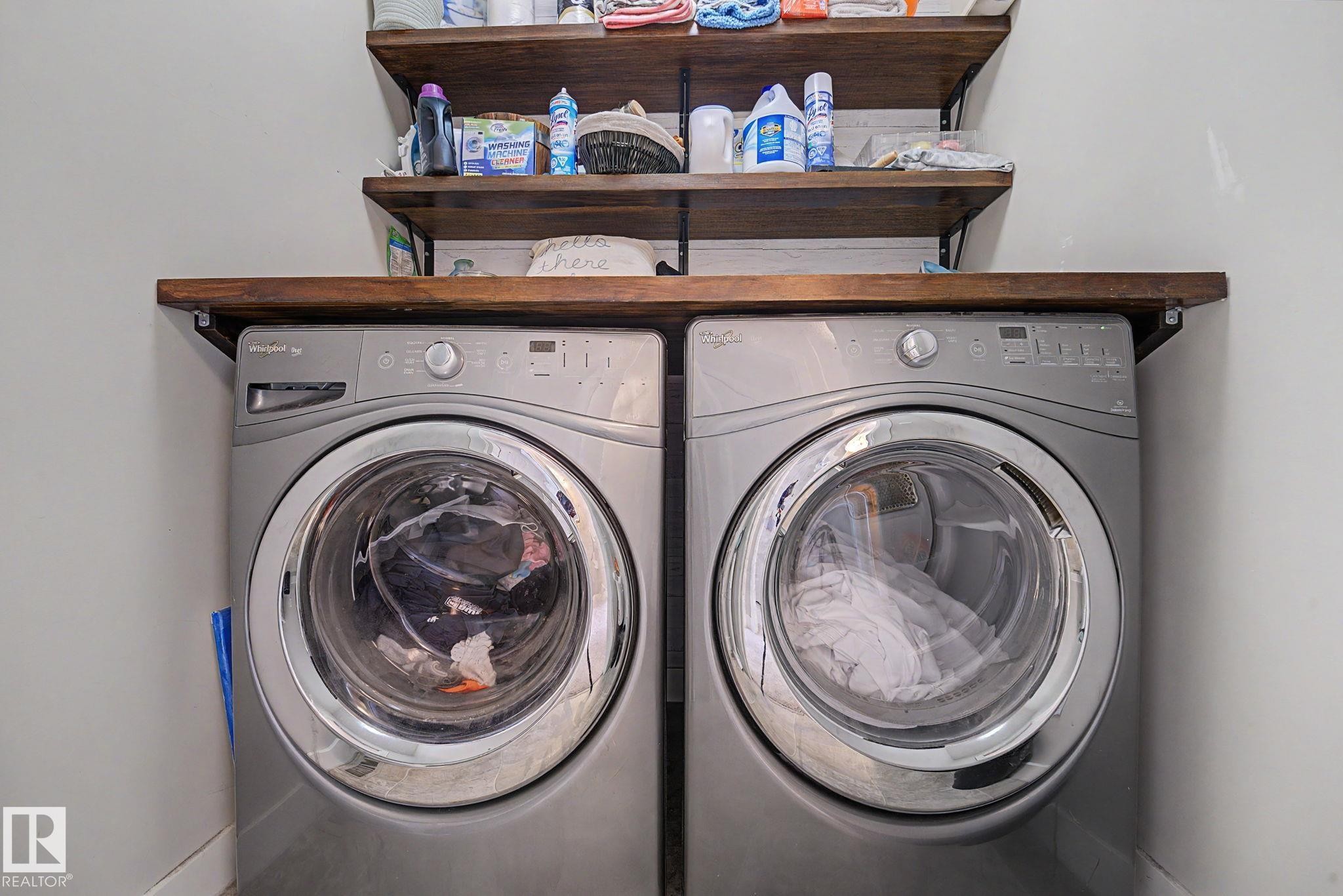 Integrated laundry area featuring two front-loading machines, a wood-finish countertop, and two open wood-finish shelves - 3343 Weidle Way Sw, Edmonton, AB