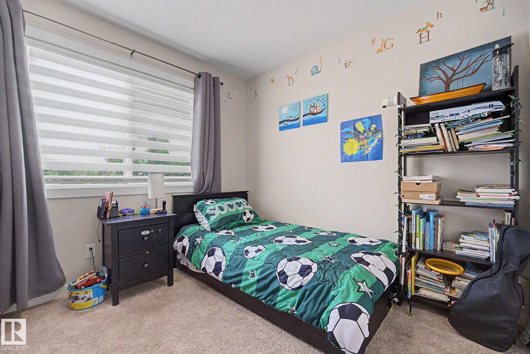Carpeted bedroom featuring a large window with horizontal blinds and full-length gray drapes - 3343 Weidle Way Sw, Edmonton, AB