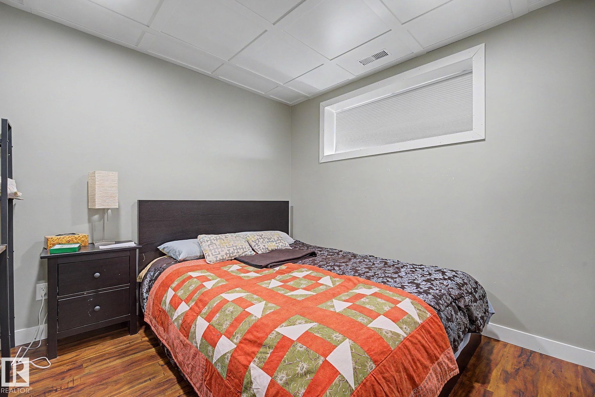 Bedroom featuring wood-finish flooring, light gray walls, a white drop ceiling, and a high horizontal window - 3343 Weidle Way Sw, Edmonton, AB