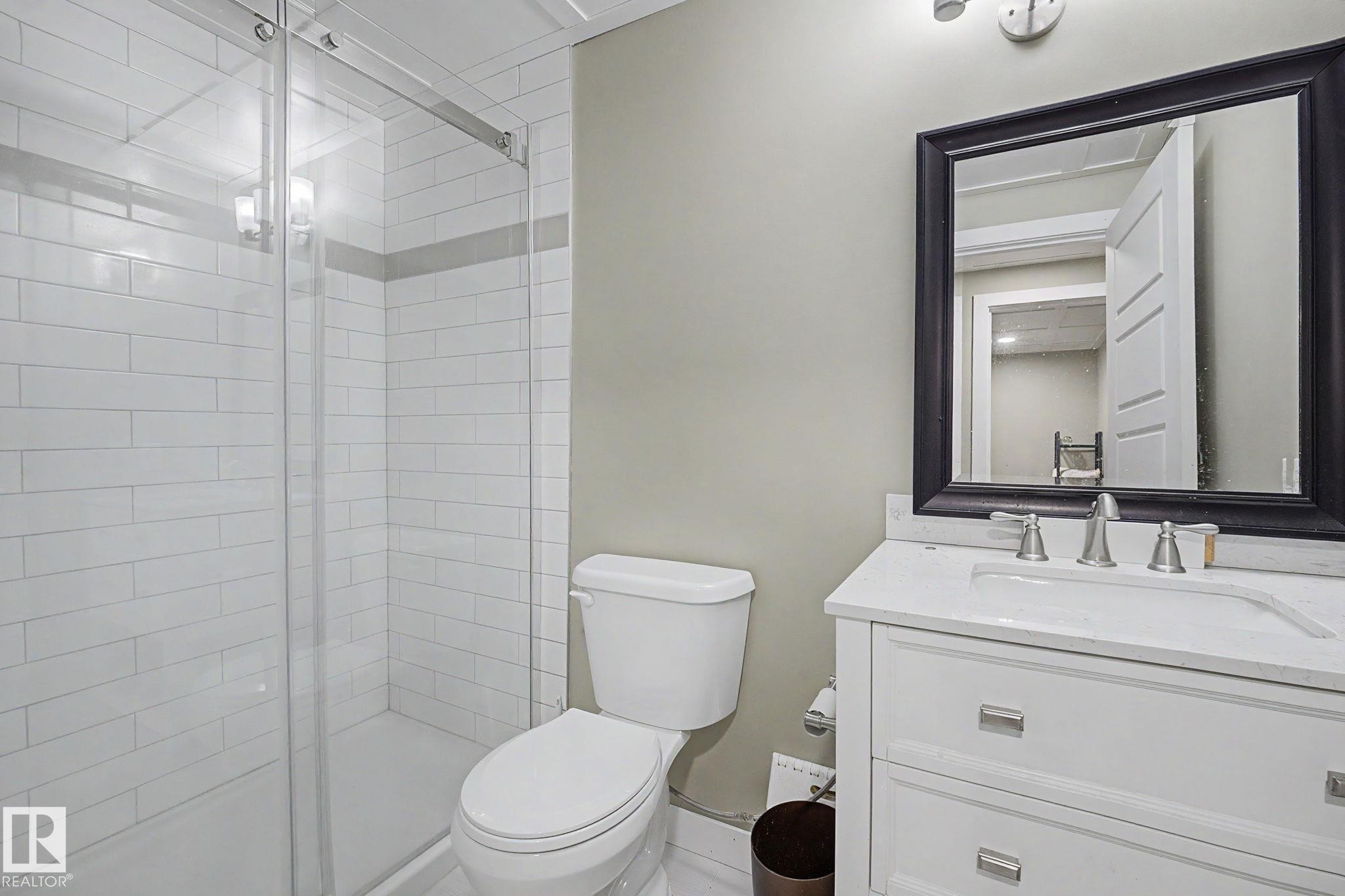 Bathroom featuring a glass-enclosed shower with subway tile surround, a single vanity with a white countertop, and a framed mirror - 3343 Weidle Way Sw, Edmonton, AB