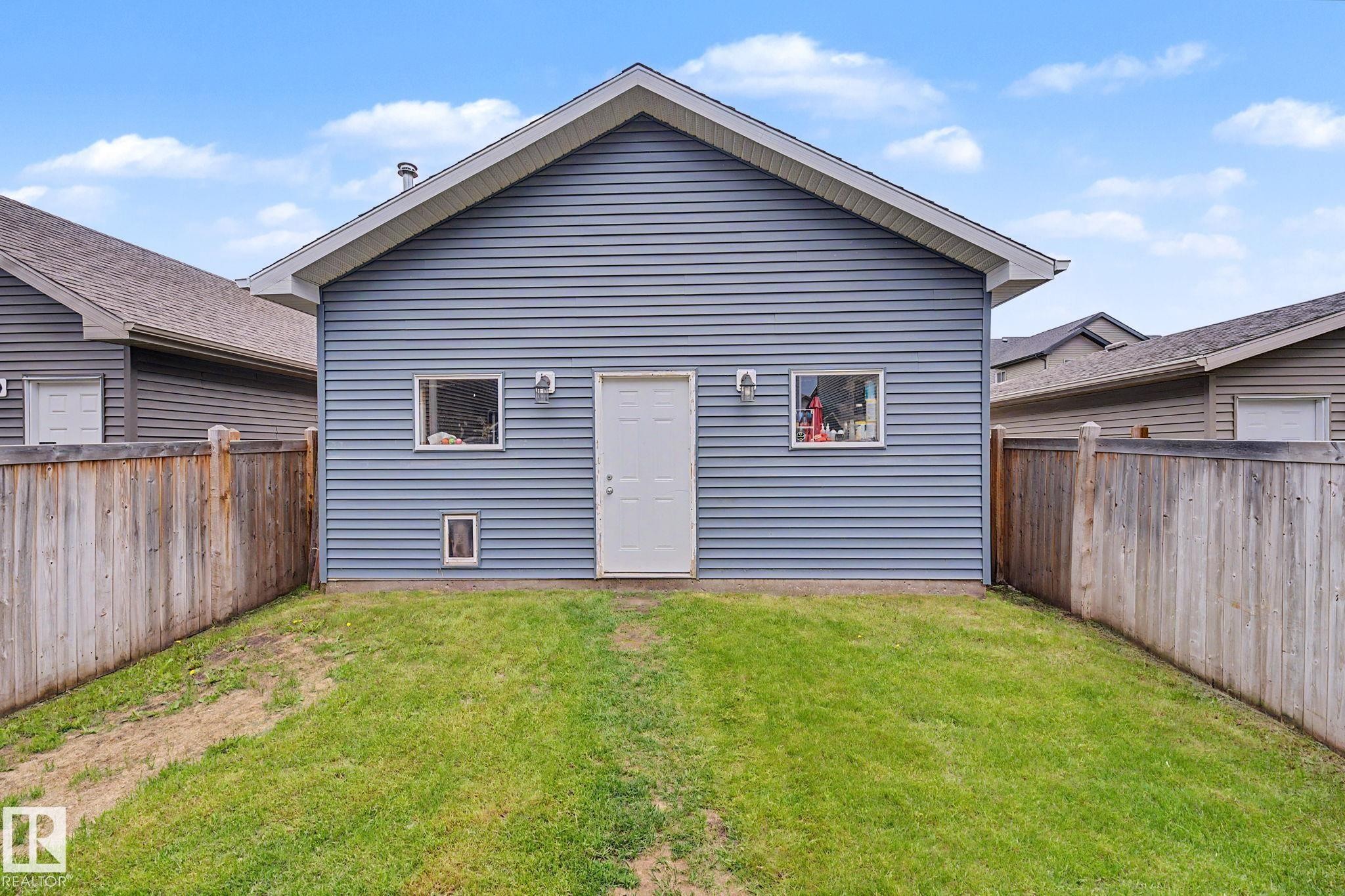 Detached garage featuring blue horizontal siding, white trim, two exterior lights, and a white access door - 3343 Weidle Way Sw, Edmonton, AB