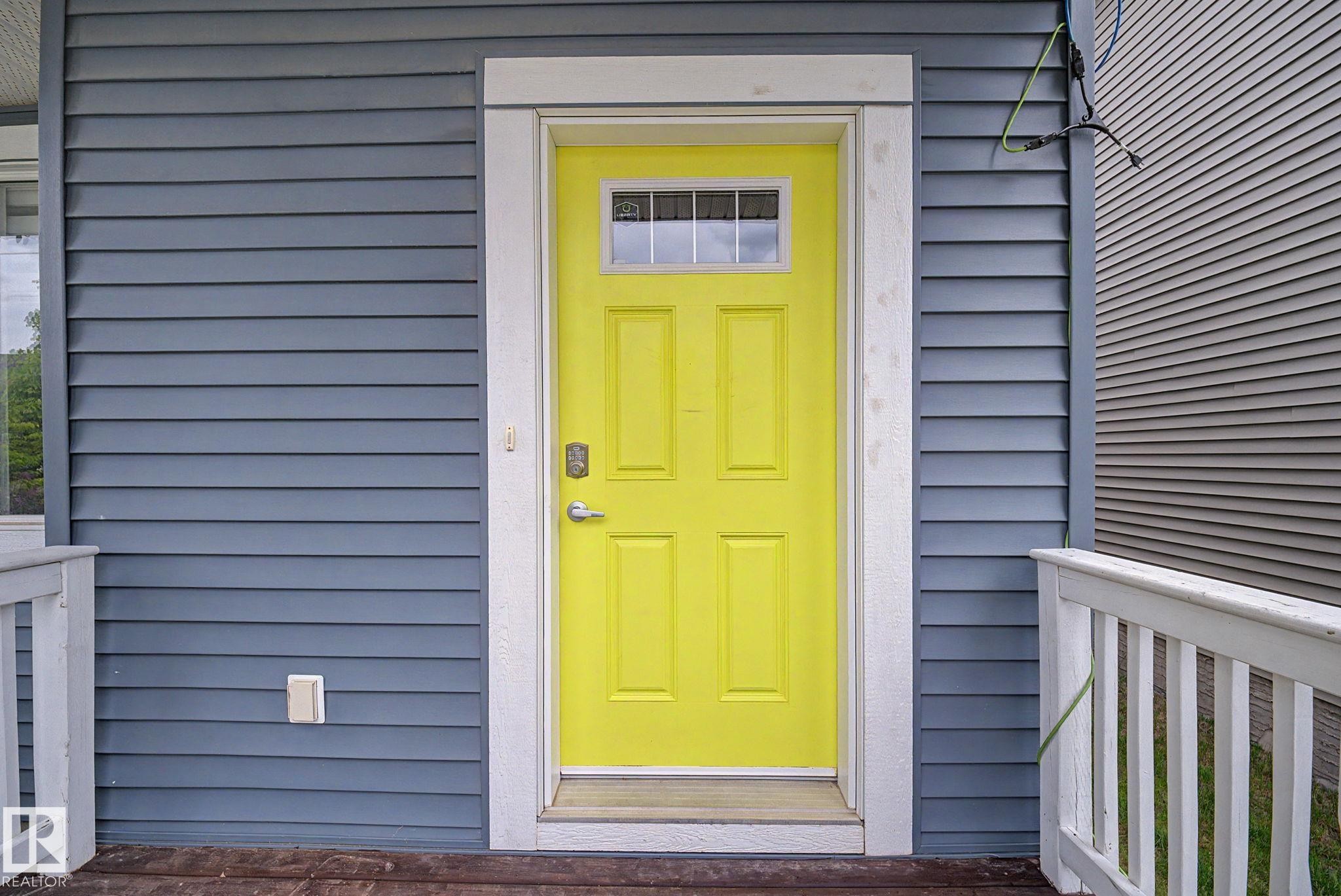 Bold yellow entry door with transom window set against horizontal gray siding - 3343 Weidle Way Sw, Edmonton, AB