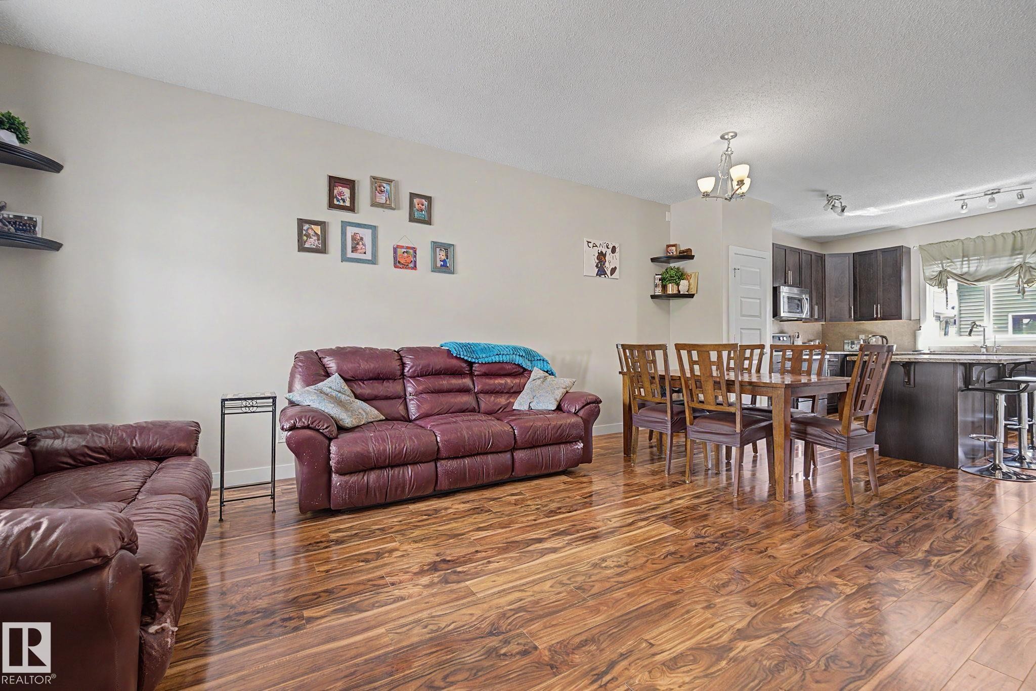 Open-concept living space featuring wood-finish flooring, recessed lighting, and a dining area with a contemporary chandelier - 3343 Weidle Way Sw, Edmonton, AB
