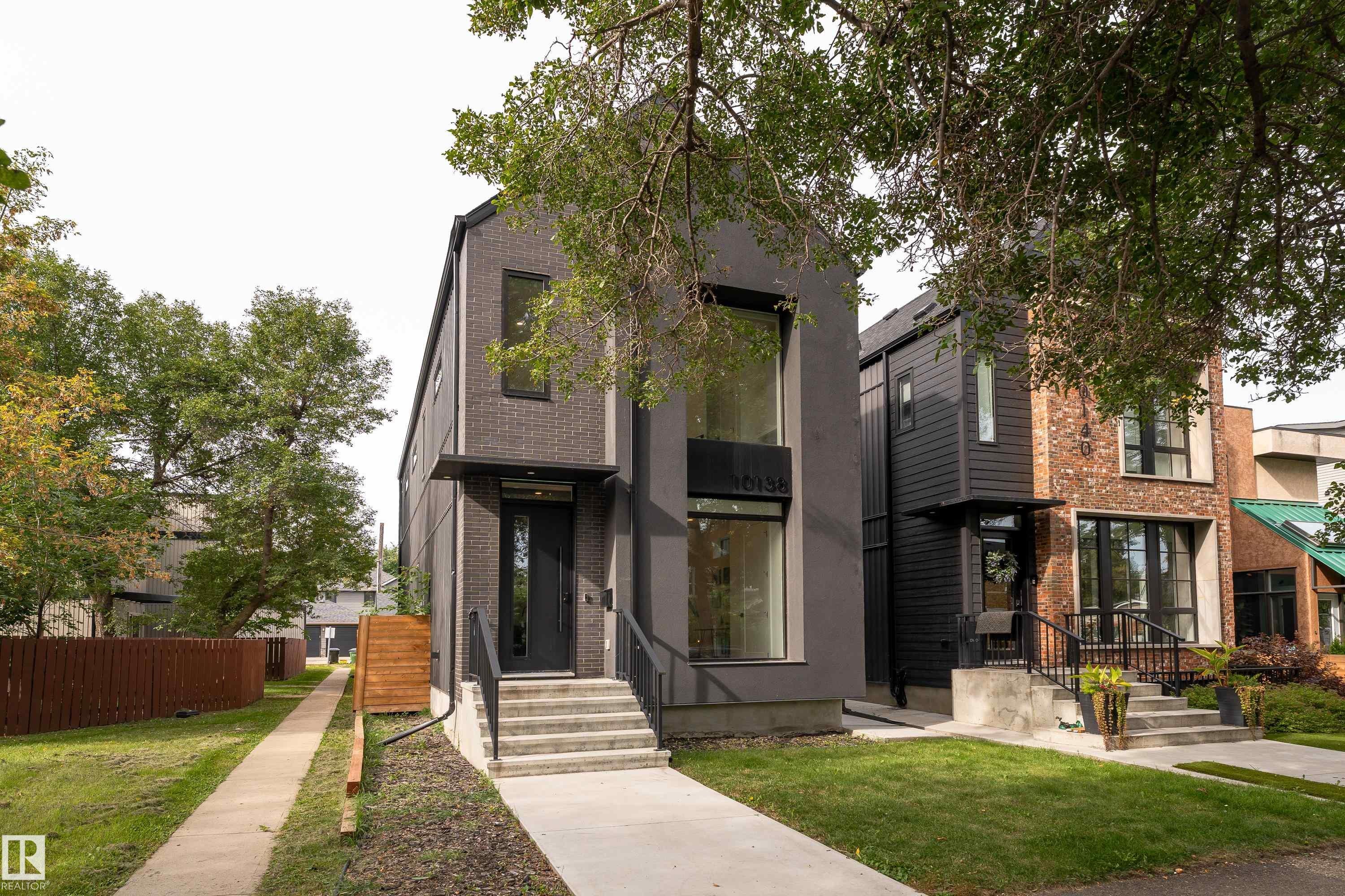 Modern facade featuring dark brick and smooth paneling, large windows, and a prominent front entry with an awning - 10138 90 Street Nw, Edmonton, AB