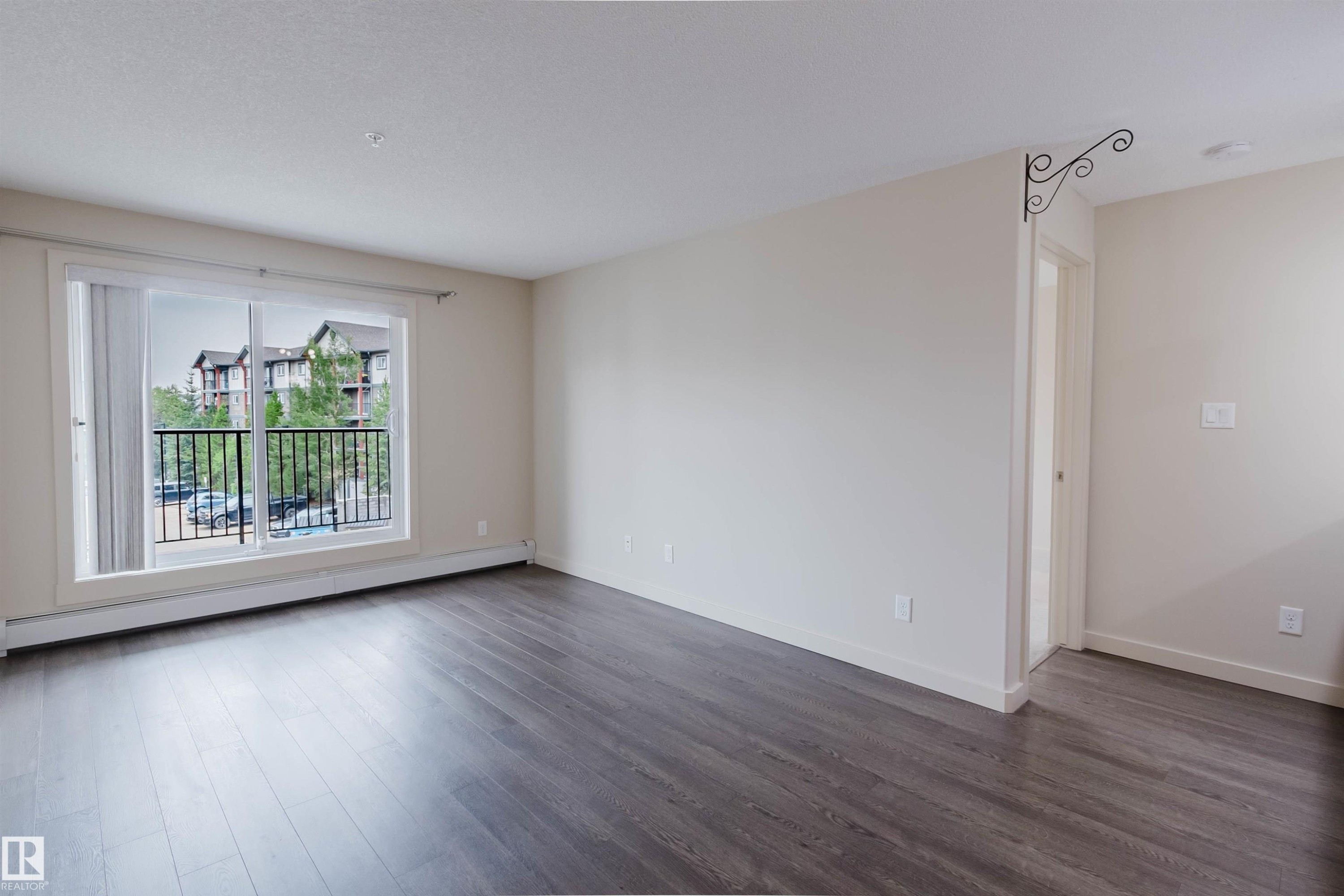 Open-concept living space featuring wood-finish flooring, neutral wall tones, and white baseboards - #304 6084 Stanton Dr Sw, Edmonton, AB - Indoor