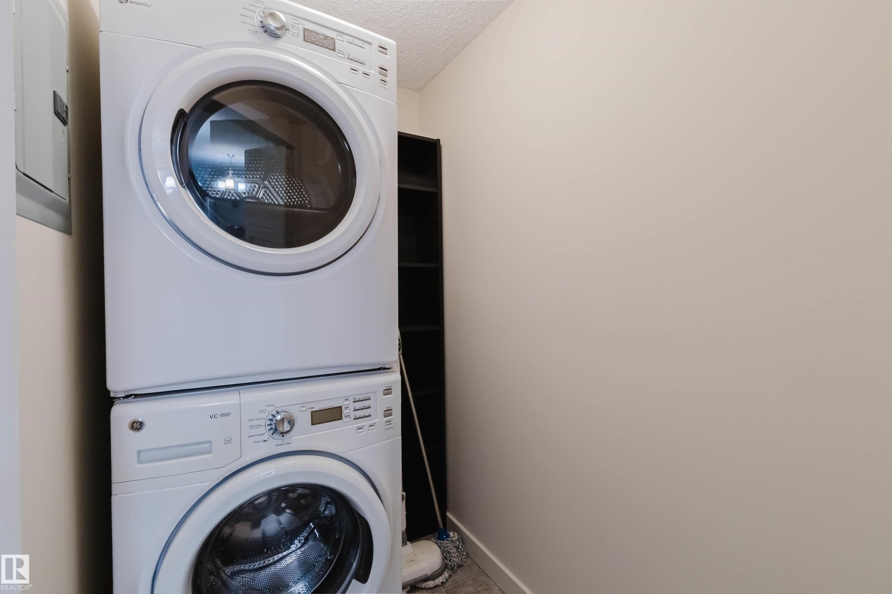 Laundry area featuring a stacked washer and dryer, light-toned wall paint, and a textured ceiling - #304 6084 Stanton Dr Sw, Edmonton, AB - Indoor Photo Showing Laundry Room