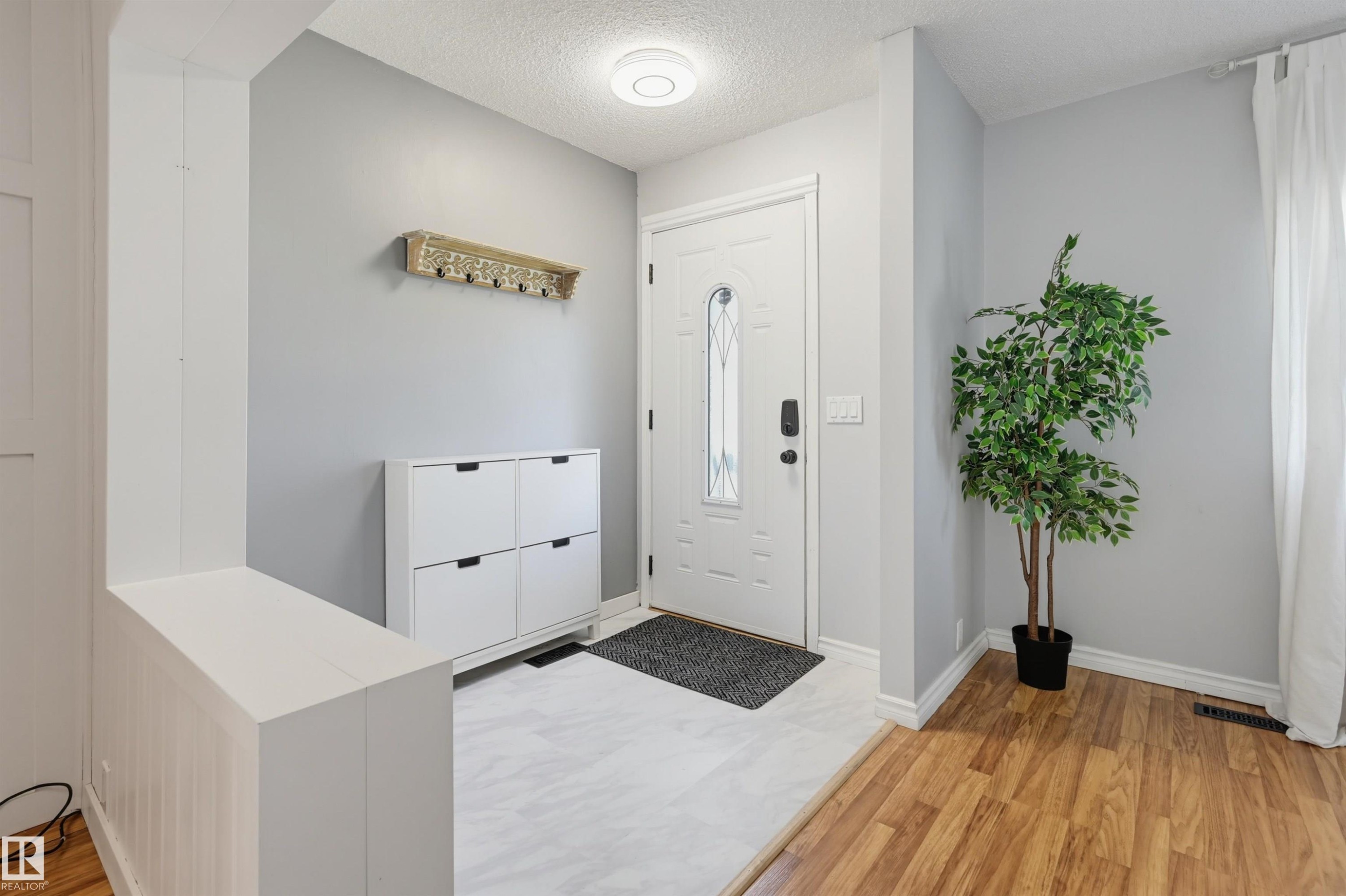 Foyer featuring a white entry door with decorative glass inserts, white baseboards, and a combination of wood-finish flooring and light-toned tile flooring - 4125 38 Street Nw, Edmonton, AB