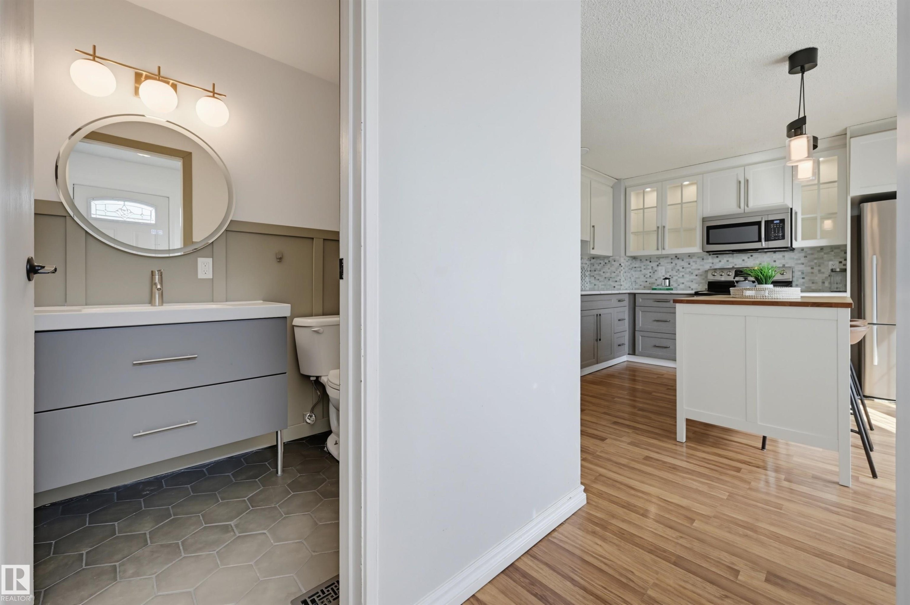 Modern kitchen with white upper and gray lower cabinetry, stainless steel appliances, and wood-finish flooring - 4125 38 Street Nw, Edmonton, AB