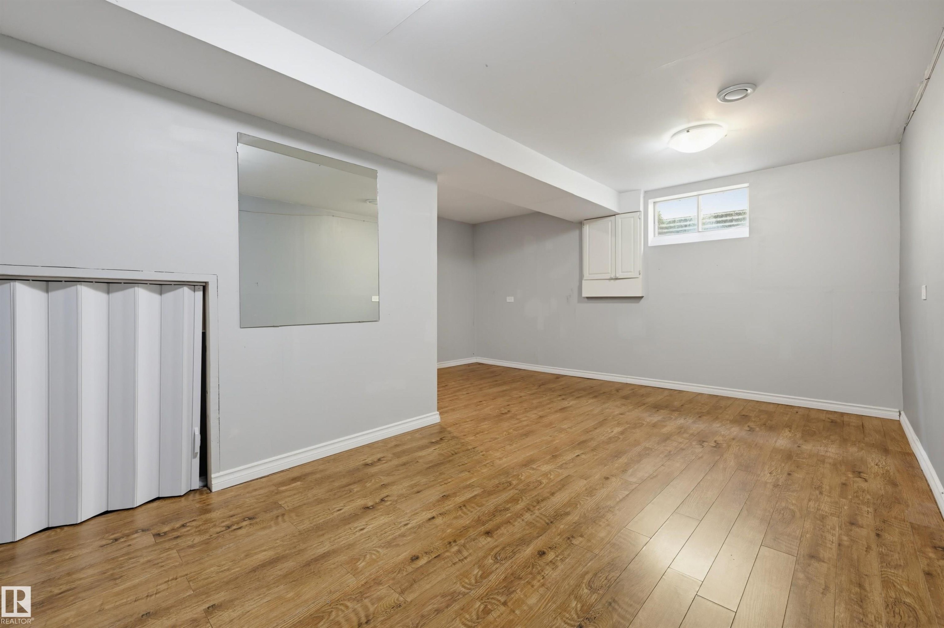 Expansive room featuring wood-finish flooring, a contemporary ceiling light fixture, and a built-in wall cabinet - 4125 38 Street Nw, Edmonton, AB