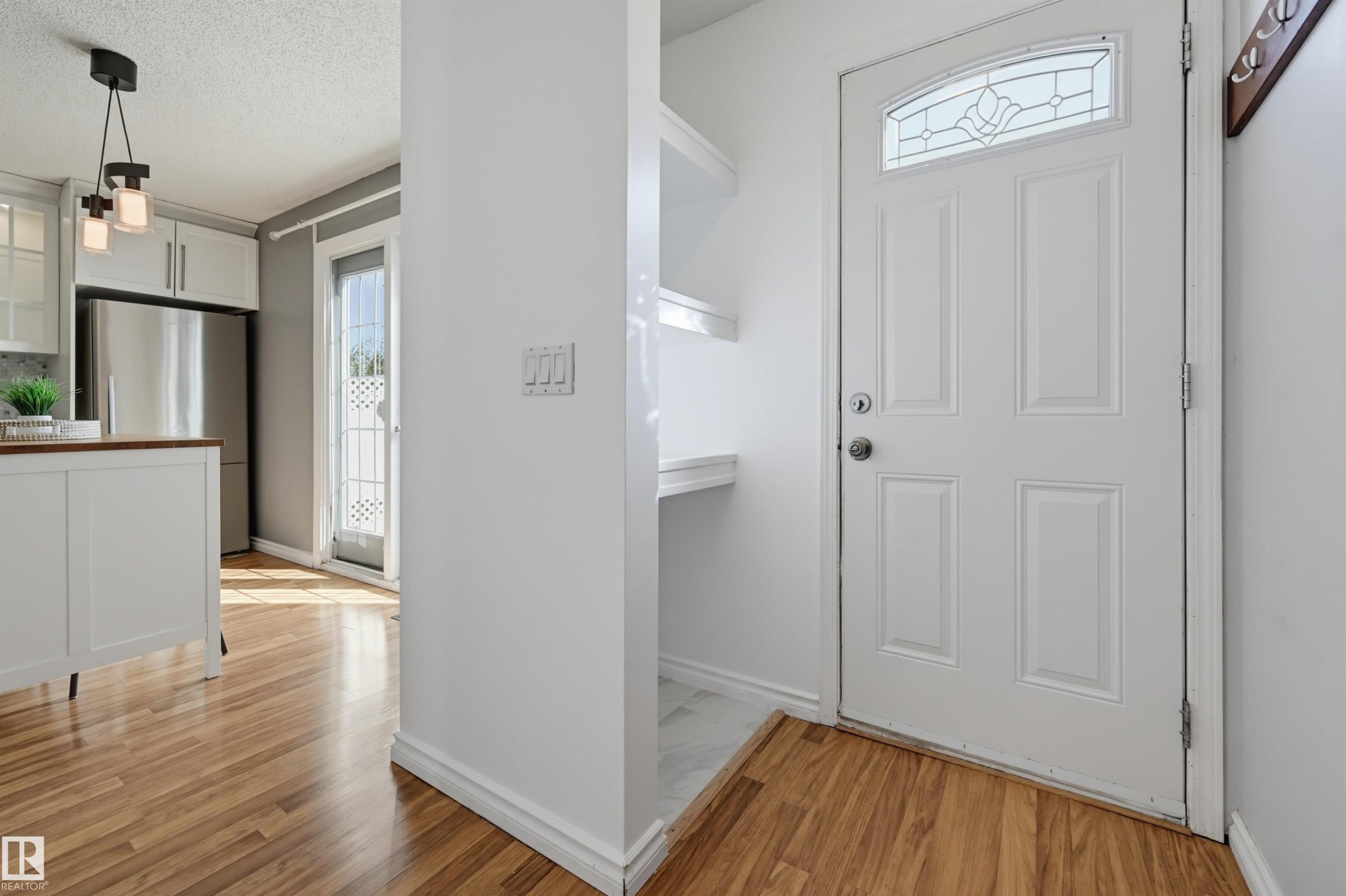 Wood-finish flooring throughout, white paneled door with decorative glass insert, and built-in shelving - 4125 38 Street Nw, Edmonton, AB