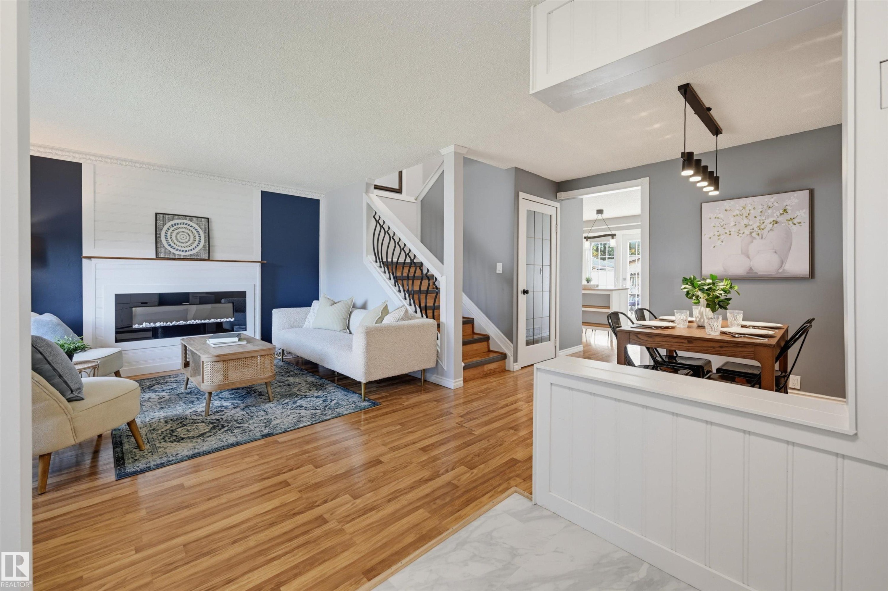 Wood-finish flooring throughout, modern fireplace with white mantel, custom staircase with wrought iron detailing, built-in dining area lighting, and a glass-paneled interior door - 4125 38 Street Nw, Edmonton, AB