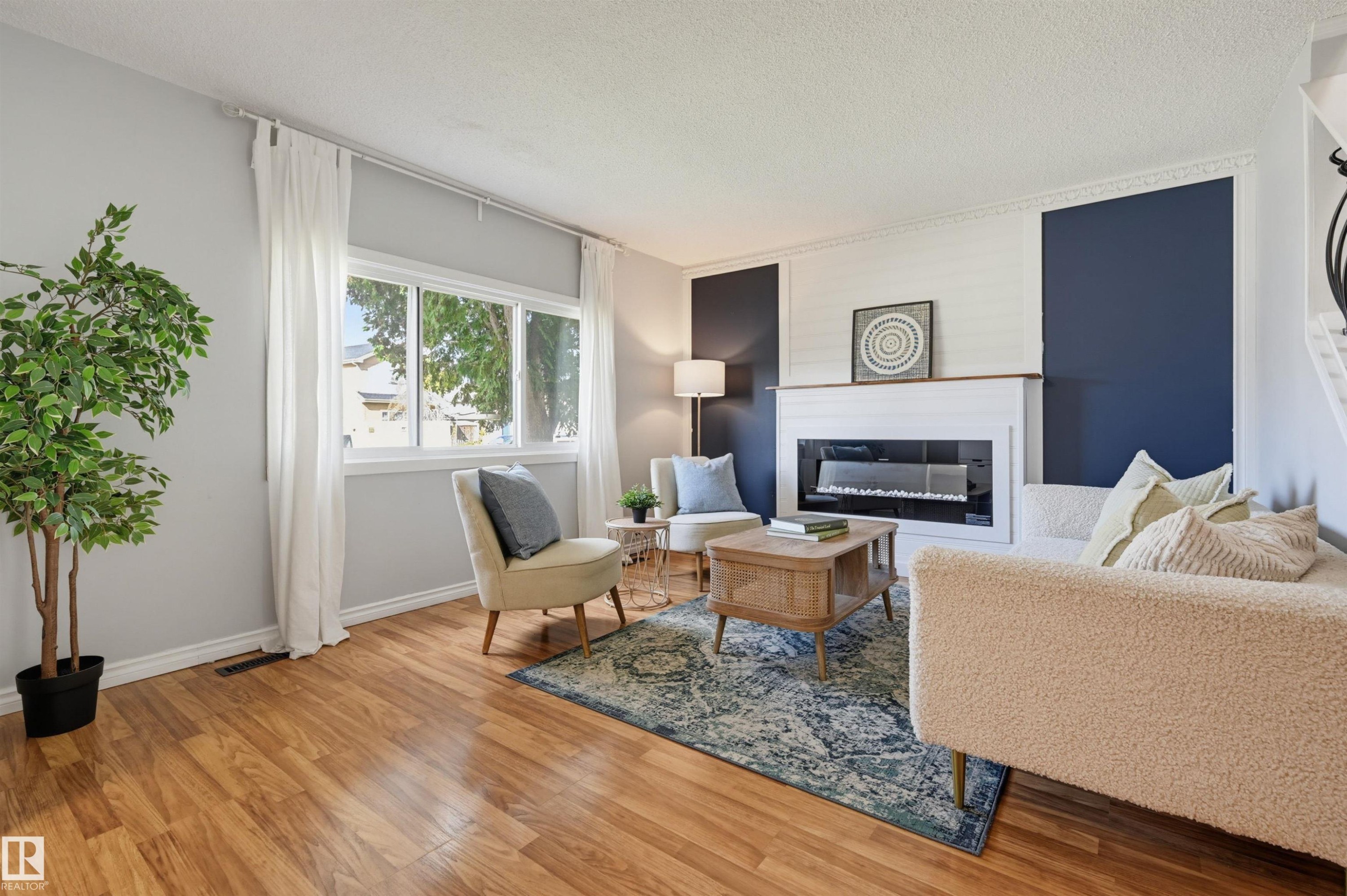 Wood-finish flooring, large multi-pane window, electric fireplace, white mantel, and architectural accent wall - 4125 38 Street Nw, Edmonton, AB
