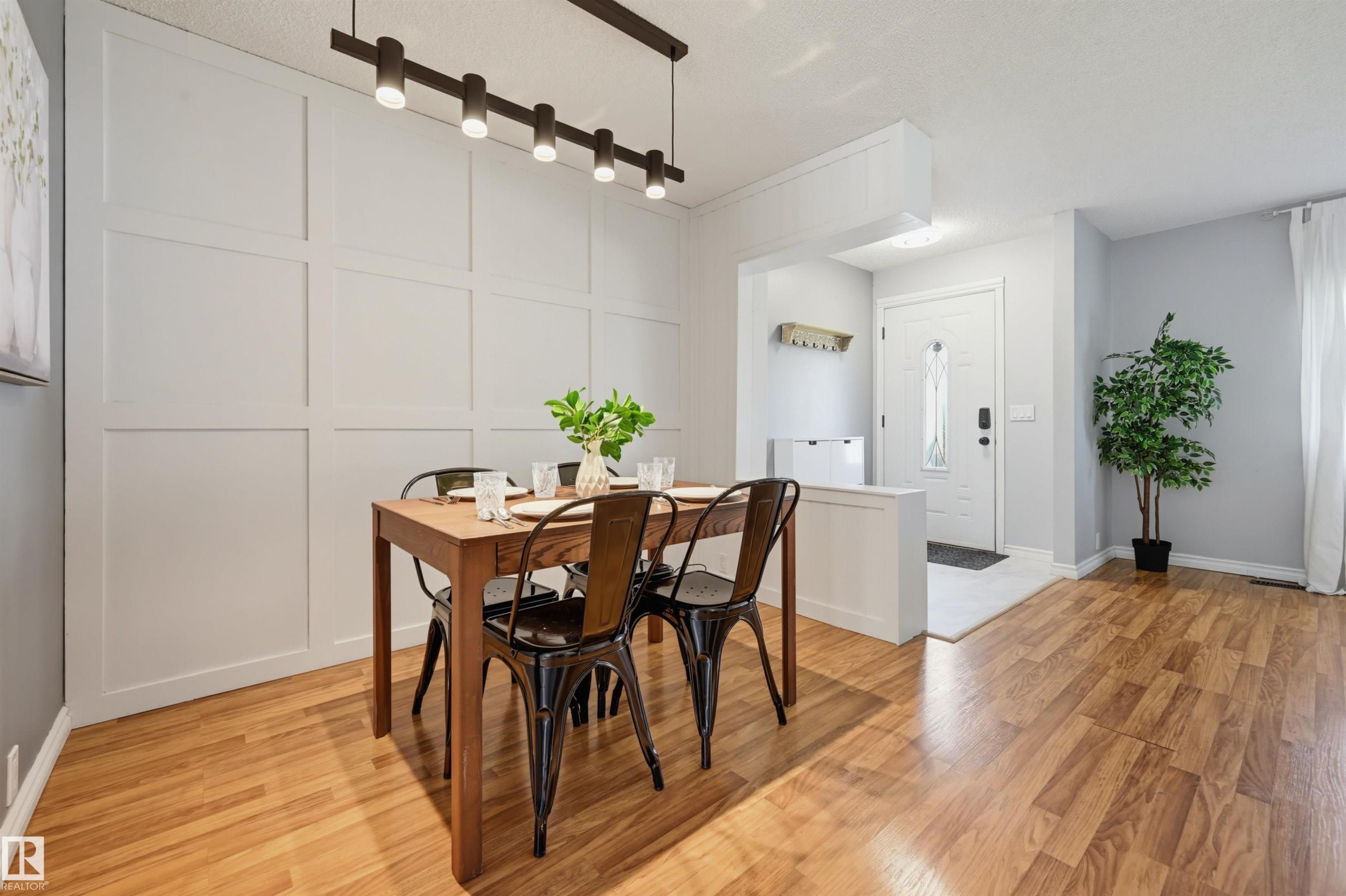 Wood-finish flooring, accent wall with paneling, modern track lighting fixture, white entry door with frosted glass, and a built-in partition wall - 4125 38 Street Nw, Edmonton, AB