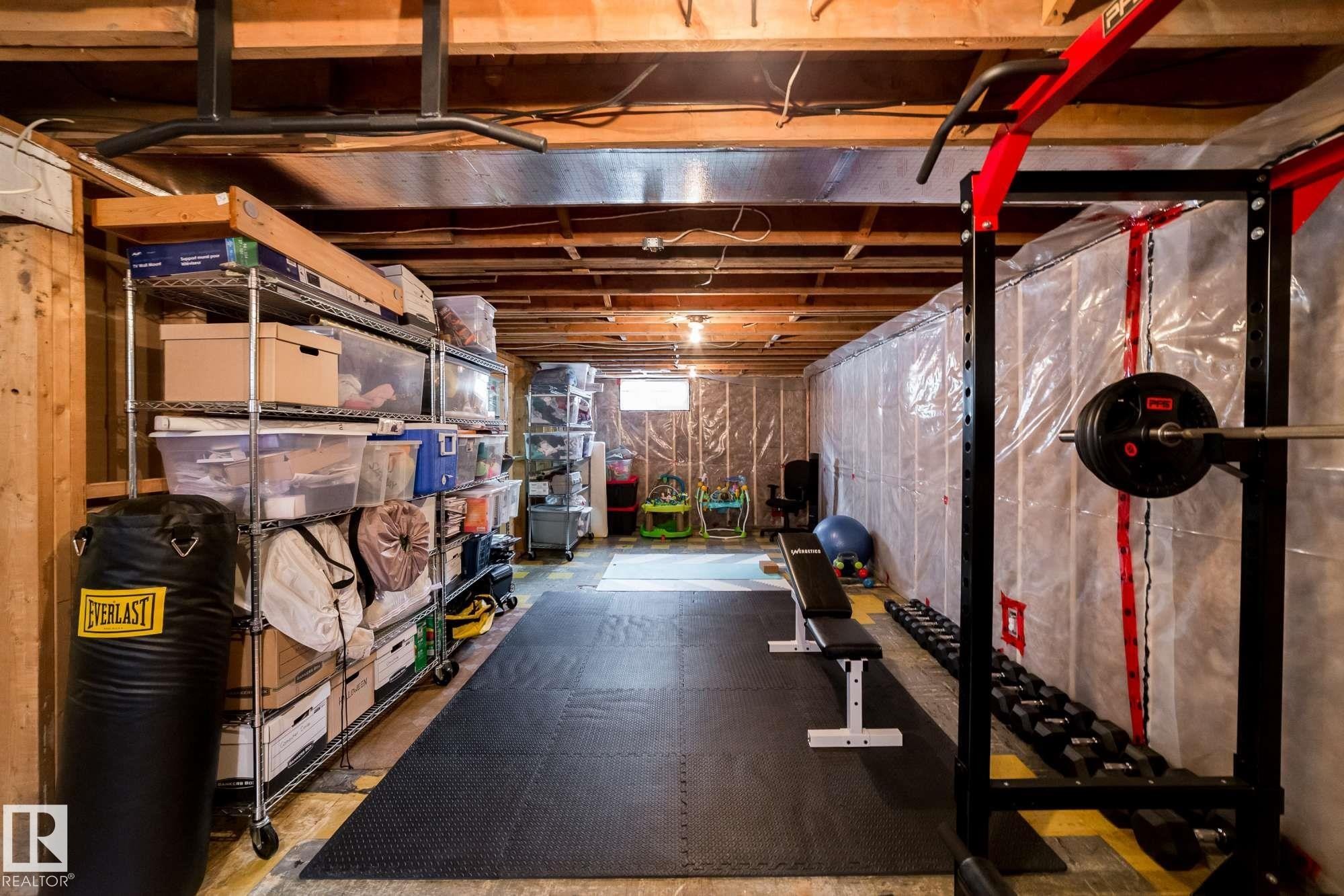 Finished basement area with exposed ceiling joists, durable rubber flooring, and ample built-in shelving - 12228 134 Street Nw, Edmonton, AB