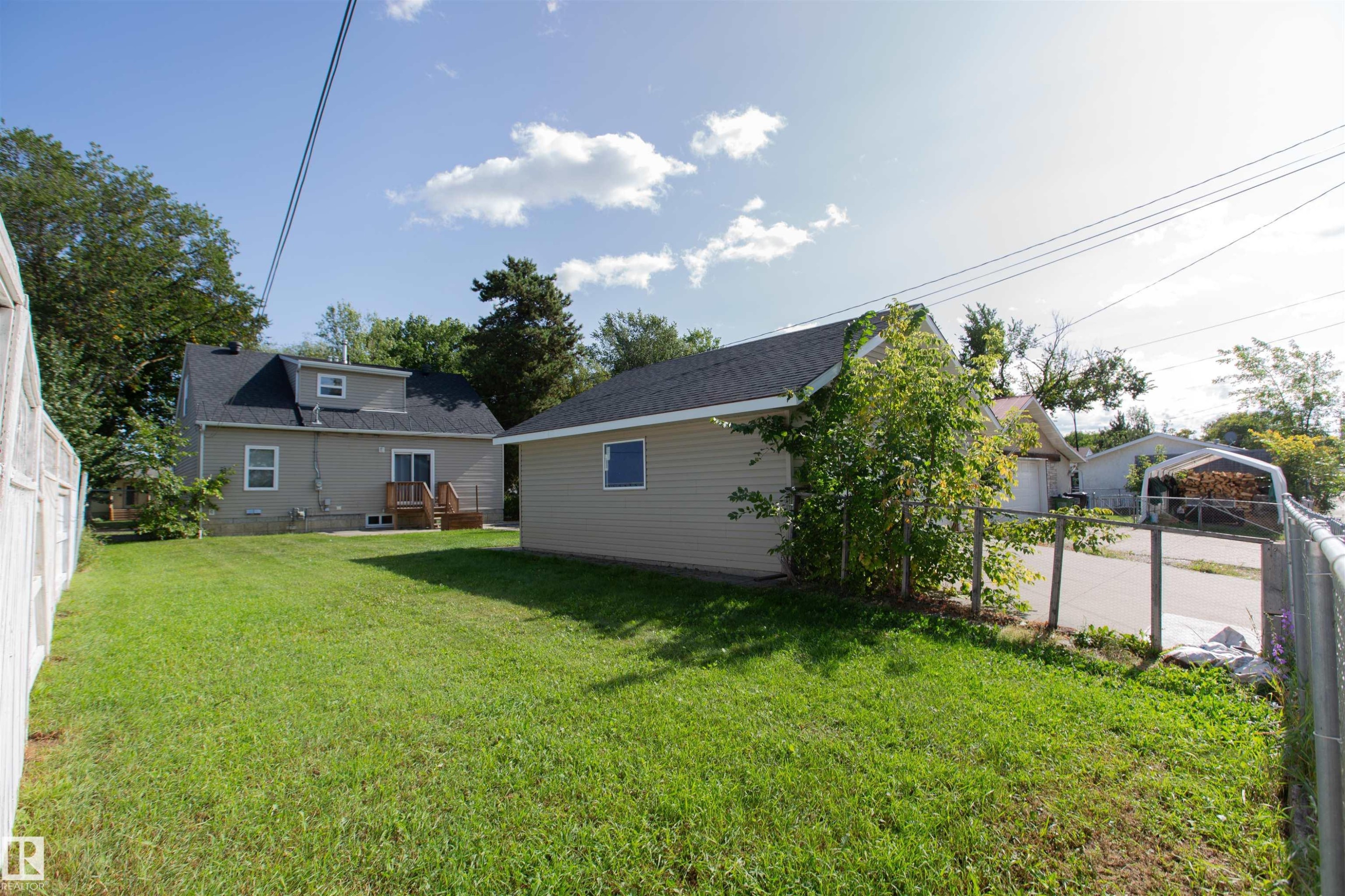 Expansive green lawn with a detached building, chain link fencing, a wooden deck, and mature trees - 12228 134 Street Nw, Edmonton, AB