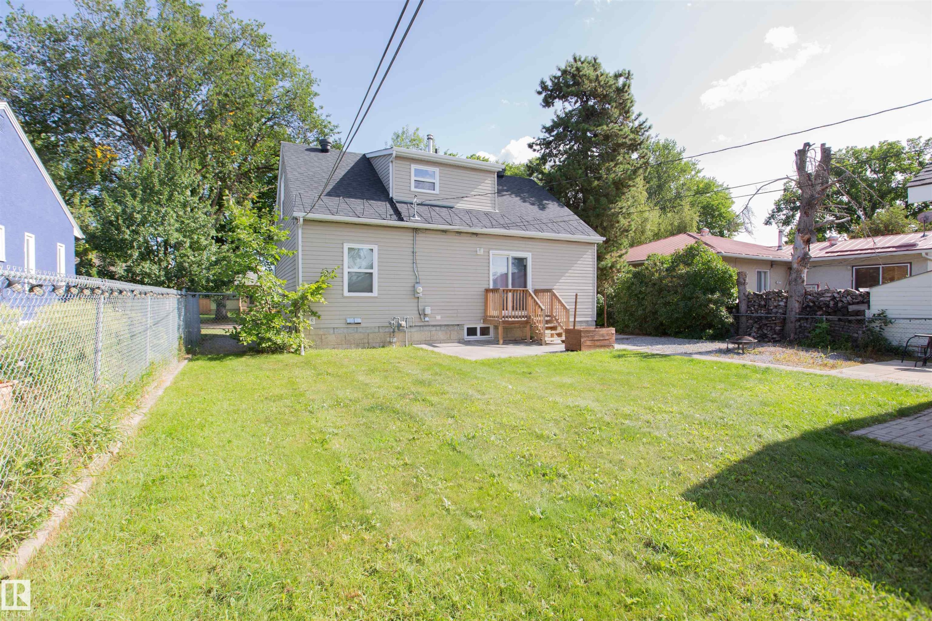 Expansive grassy yard with concrete patio, wood deck, and chain-link fencing - 12228 134 Street Nw, Edmonton, AB