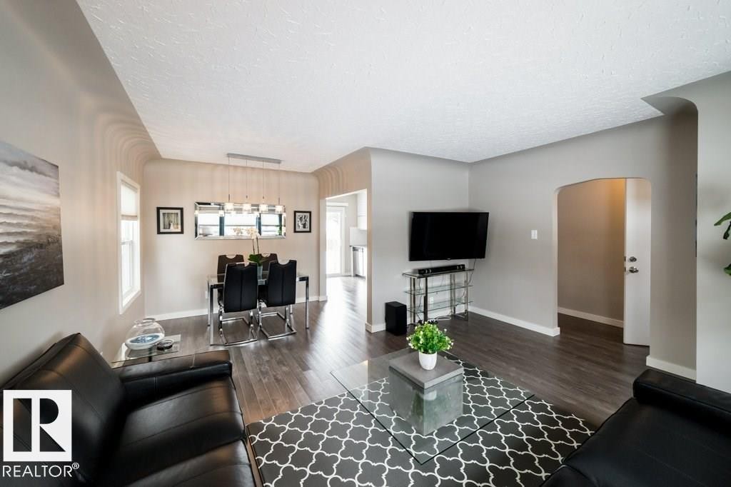 Open-concept living area with wood-finish flooring, a dining space with a linear pendant light, and an arched doorway - 12228 134 Street Nw, Edmonton, AB