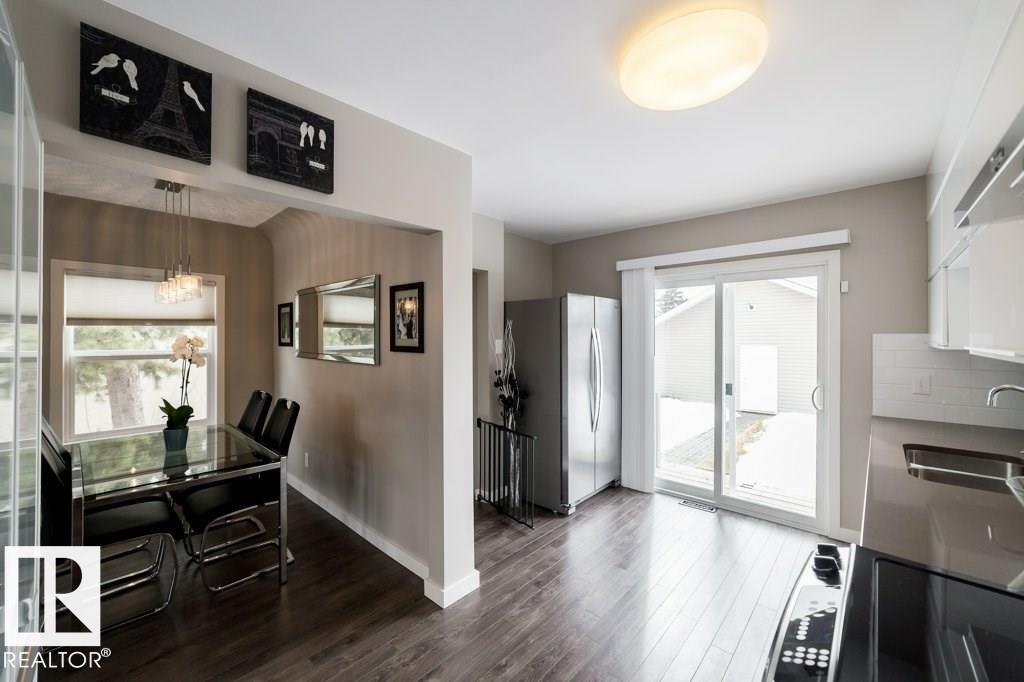 Wood-finish flooring throughout, kitchen with white cabinetry, stainless steel refrigerator, and subway tile backsplash - 12228 134 Street Nw, Edmonton, AB
