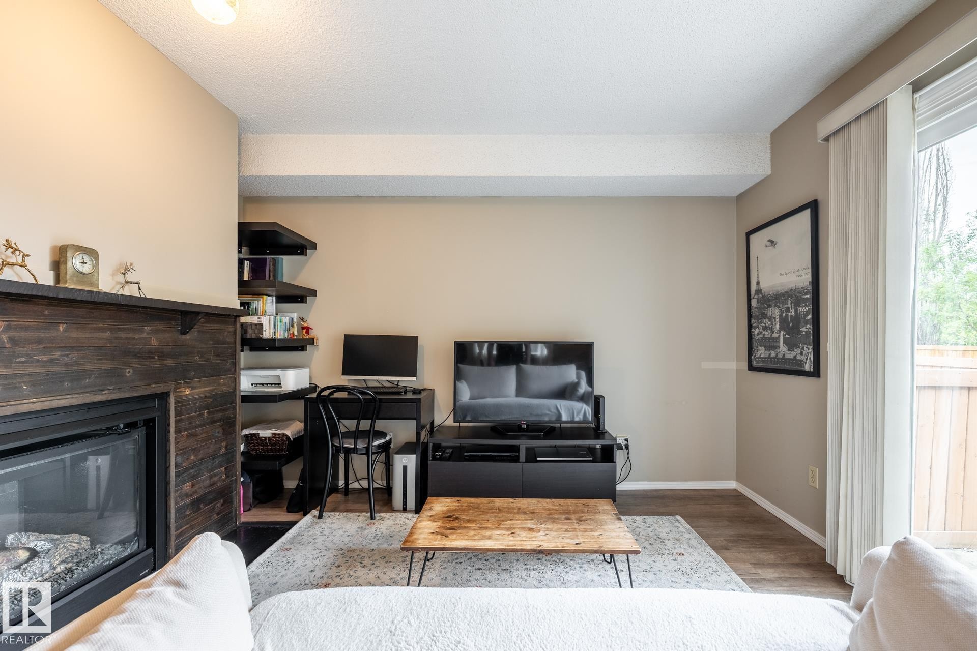 Living area featuring a gas fireplace with a dark wood-finish mantel and surround, wood-finish flooring, and built-in shelving - #20 3812 20 Av Nw, Edmonton, AB
