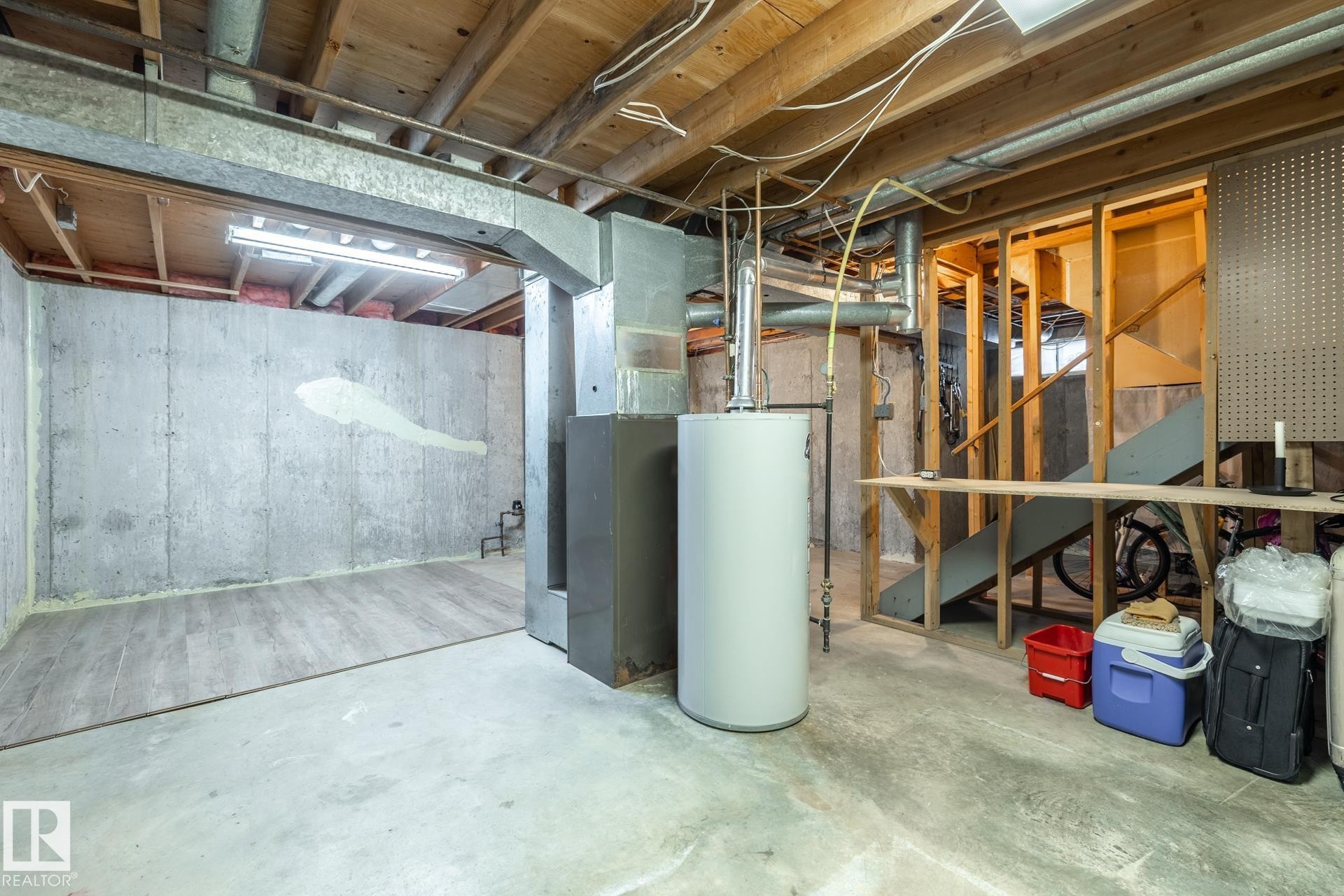 Unfinished basement space featuring exposed wood joists, concrete walls, a water heater, and a utility staircase - #20 3812 20 Av Nw, Edmonton, AB
