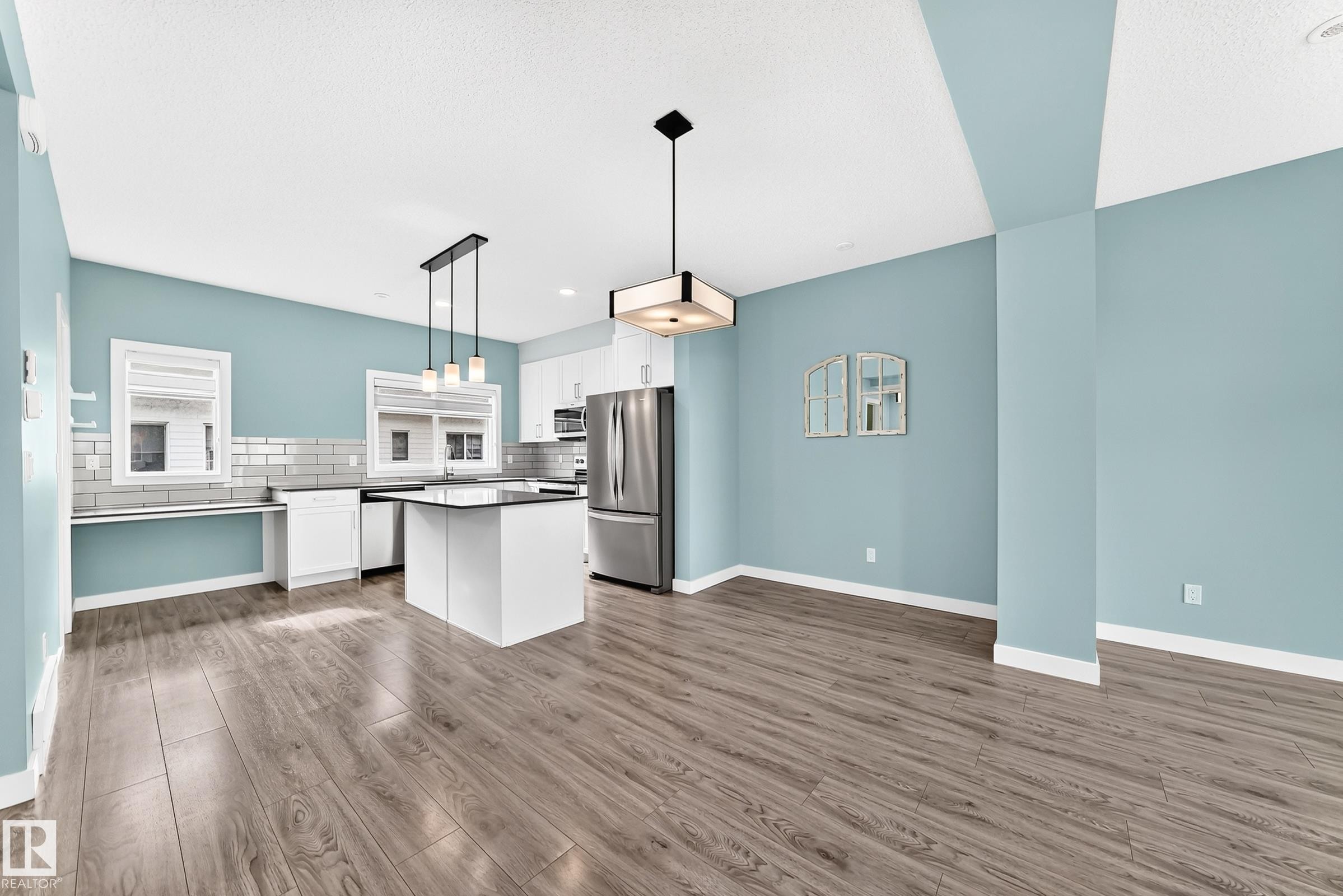 Open-concept living space with wood-finish flooring, a kitchen island, white cabinetry, and stainless steel appliances - #56 804 Welsh Dr Sw, Edmonton, AB