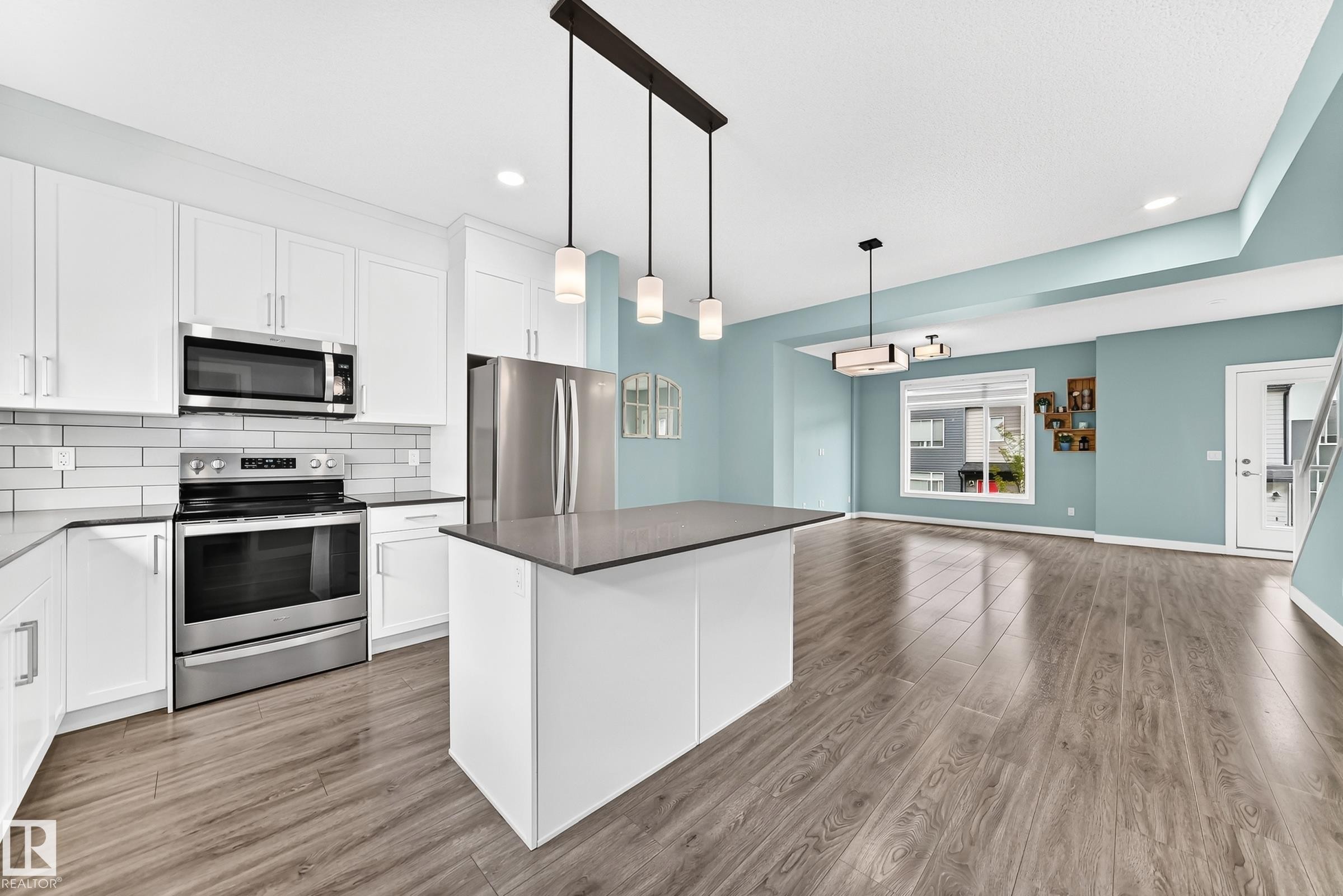 White shaker cabinetry, stainless steel appliances, a kitchen island with a dark countertop, wood-finish flooring, and pendant lighting - #56 804 Welsh Dr Sw, Edmonton, AB