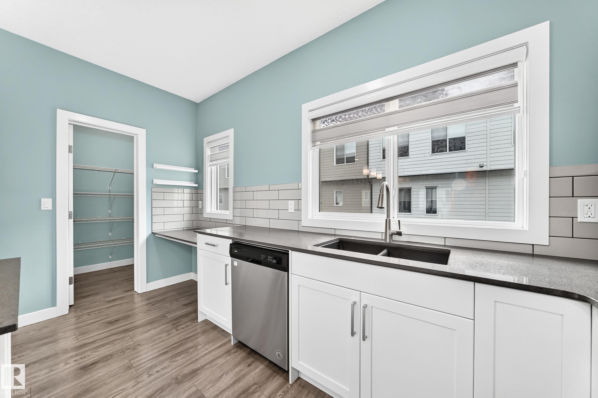 Kitchen featuring white shaker cabinetry, dark dual-basin sink, stainless steel dishwasher, and wood-finish flooring - #56 804 Welsh Dr Sw, Edmonton, AB