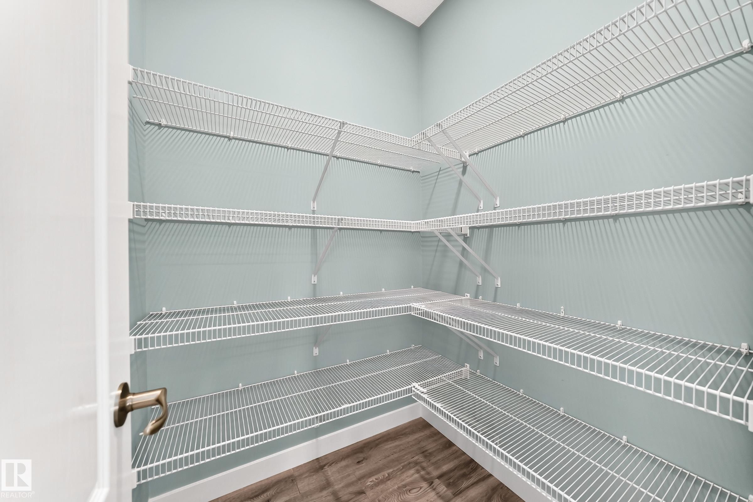 Integrated wire shelving system with multiple tiers, light blue painted walls, and wood-finish flooring - #56 804 Welsh Dr Sw, Edmonton, AB
